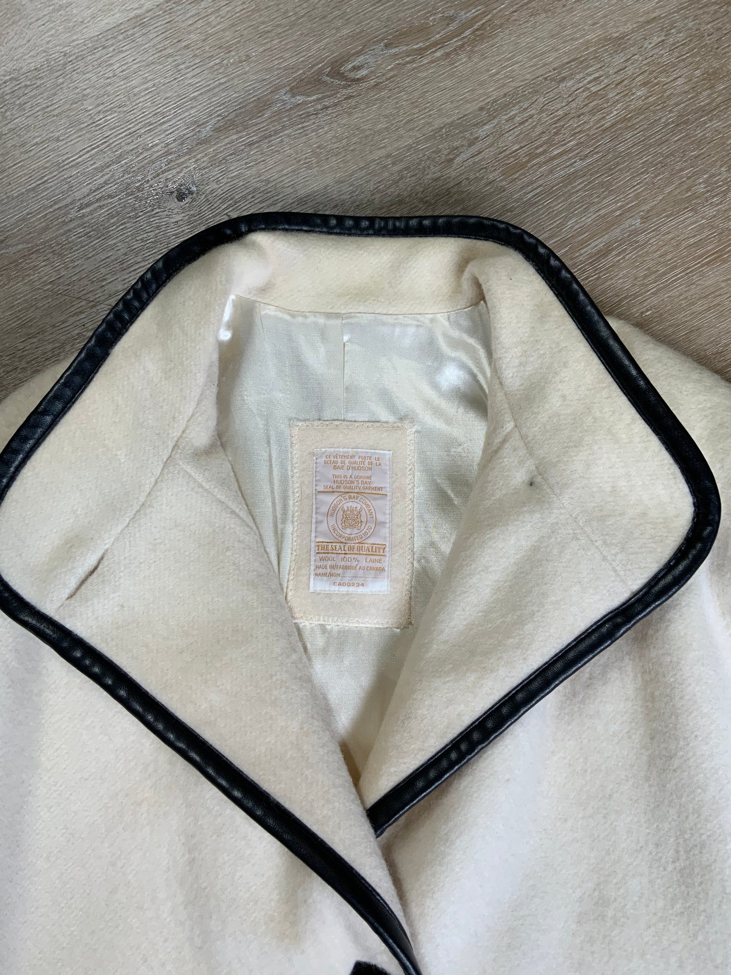 Kingspier Vintage - Genuine Hudson Bay Company 100% virgin wool coat in white with black leather trim, front pockets, flat black buttons and a unique mandarin collar with cape style detail around shoulders. Contains a Hudson’s Bay seal of quality tag. Made in Canada.
