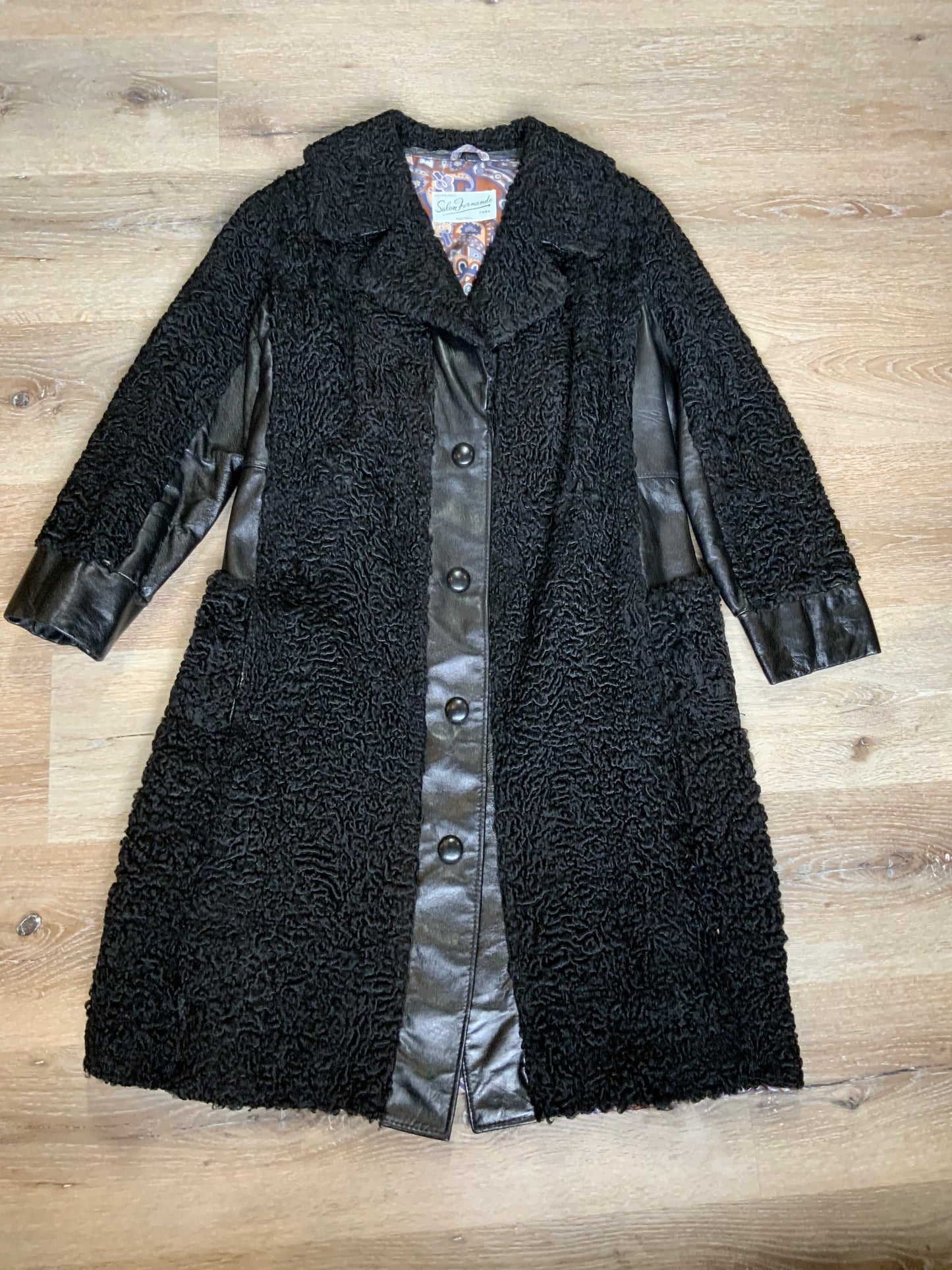 Kingspier Vintage - Salon Fernande Furs black persian wool coat with black leather trim details, four button closures down the front pockets and striking blue and bronze paisley lining with inside pockets. Made in Montreal.
