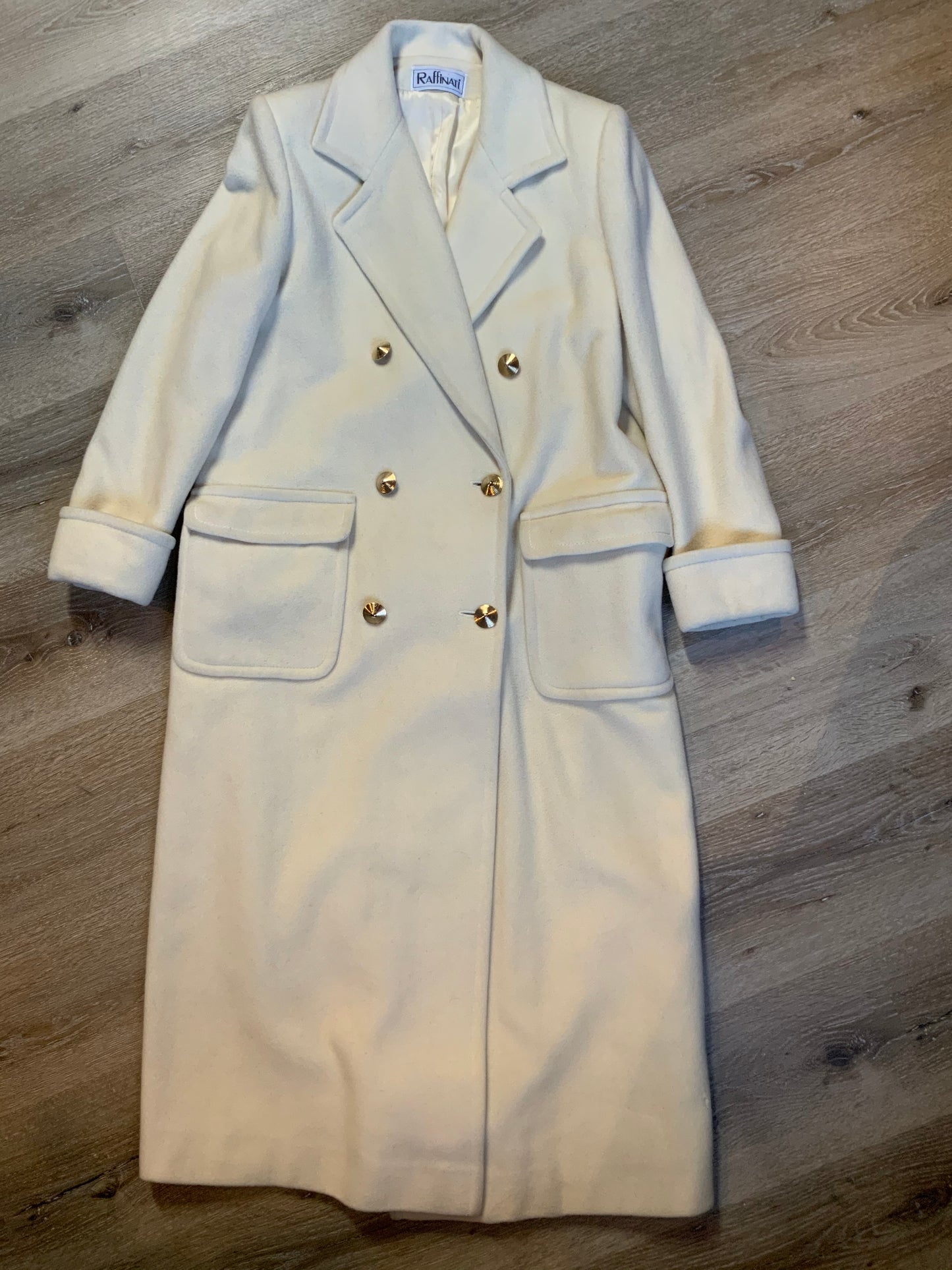 Kingspier Vintage - Raffinati 1980’s double breasted wool blend coat in cream. This coat features unique gold buttons in front, front pockets and a belt in the back. Fits a size 8.