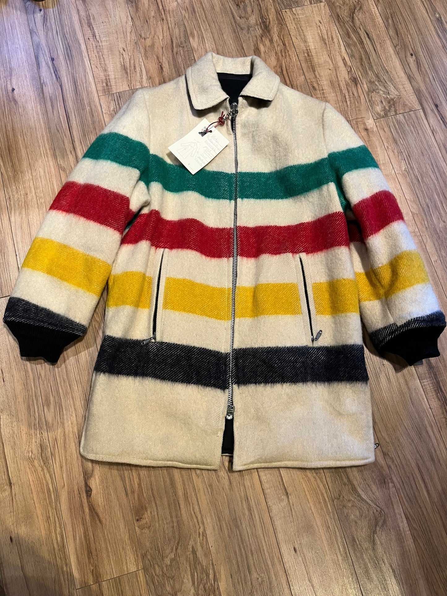 Genuine Hudson’s Bay Company 100% wool point blanket coat in the iconic multi-stripe colours. The coat features a reversible black nylon side with a hood zipped into the collar, zip pockets on both sides and knit cuffs.
Made in Canada. 
Chest measures 42”.