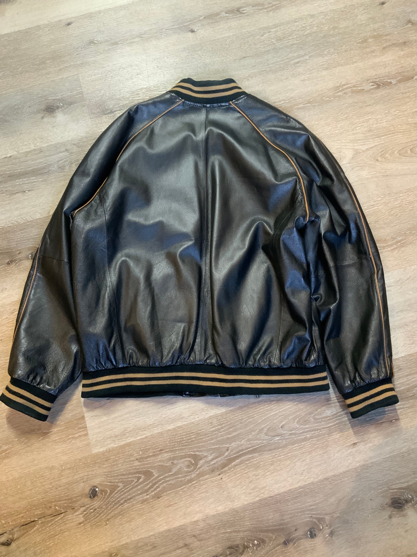 Kingspier Vintage - Retreat circa early 2000’s black leather bomber jacket with light brown stripe detailing, front zipper, slash front pockets and two inside pockets. Size 44.