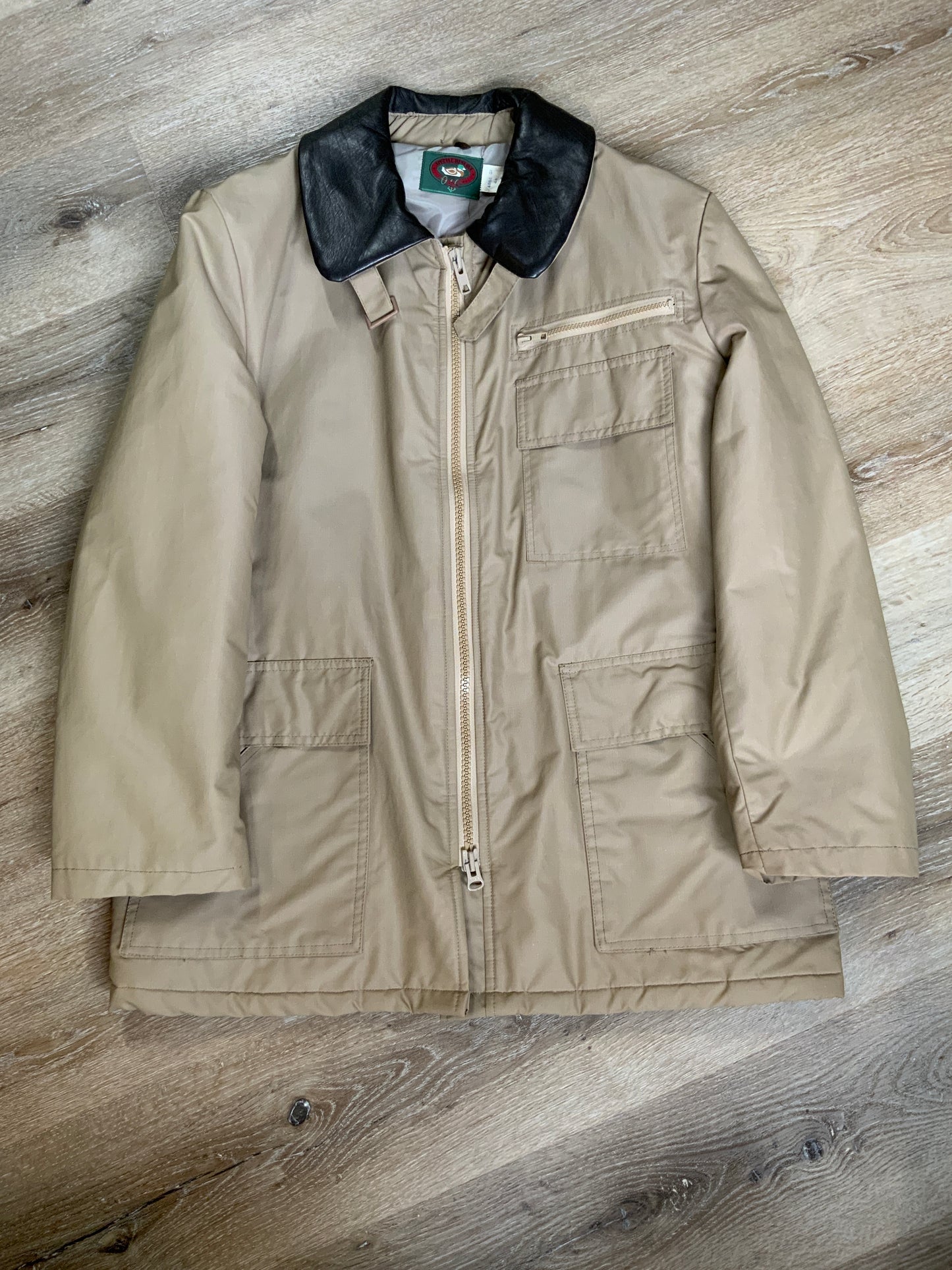 Kingspier Vintage - Special Reserve hunting jacket in beige with brown leather collar featuring a strap to keep your collar in place, zipper, three flap pockets and one zip pocket. Knit inside cuffs. lined for cooler weather with drawstring at waist. Made in Canada. Size 44.