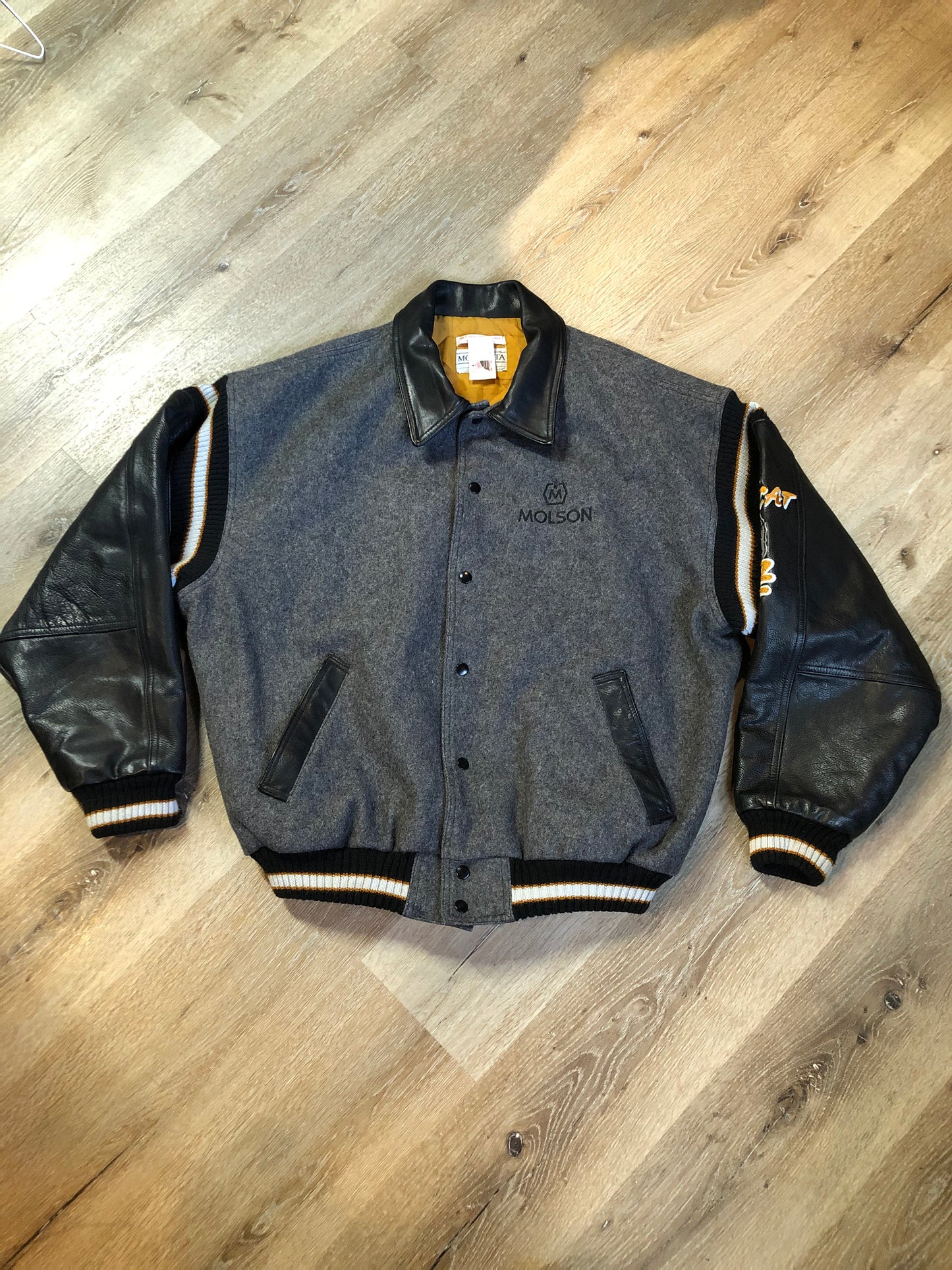 Kingspier Vintage - Fat Cat by Jazz grey and black wool varsity jacket with two large custom Jazz Golf embroidered patches on the arm and the back and Molson is embroidered on the chest in black, leather sleeves and collar, pockets, snap closures, knit details and a quilted lining. Made in Canada by Mondetta . Size XL.