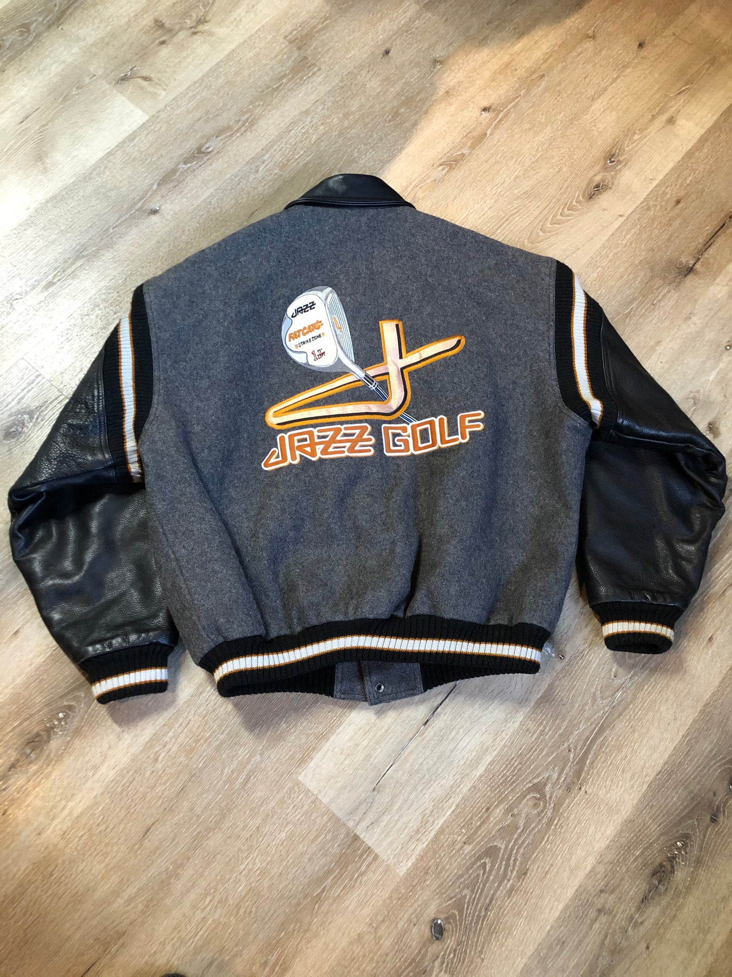 Kingspier Vintage - Fat Cat by Jazz grey and black wool varsity jacket with two large custom Jazz Golf embroidered patches on the arm and the back and Molson is embroidered on the chest in black, leather sleeves and collar, pockets, snap closures, knit details and a quilted lining. Made in Canada by Mondetta . Size XL.
