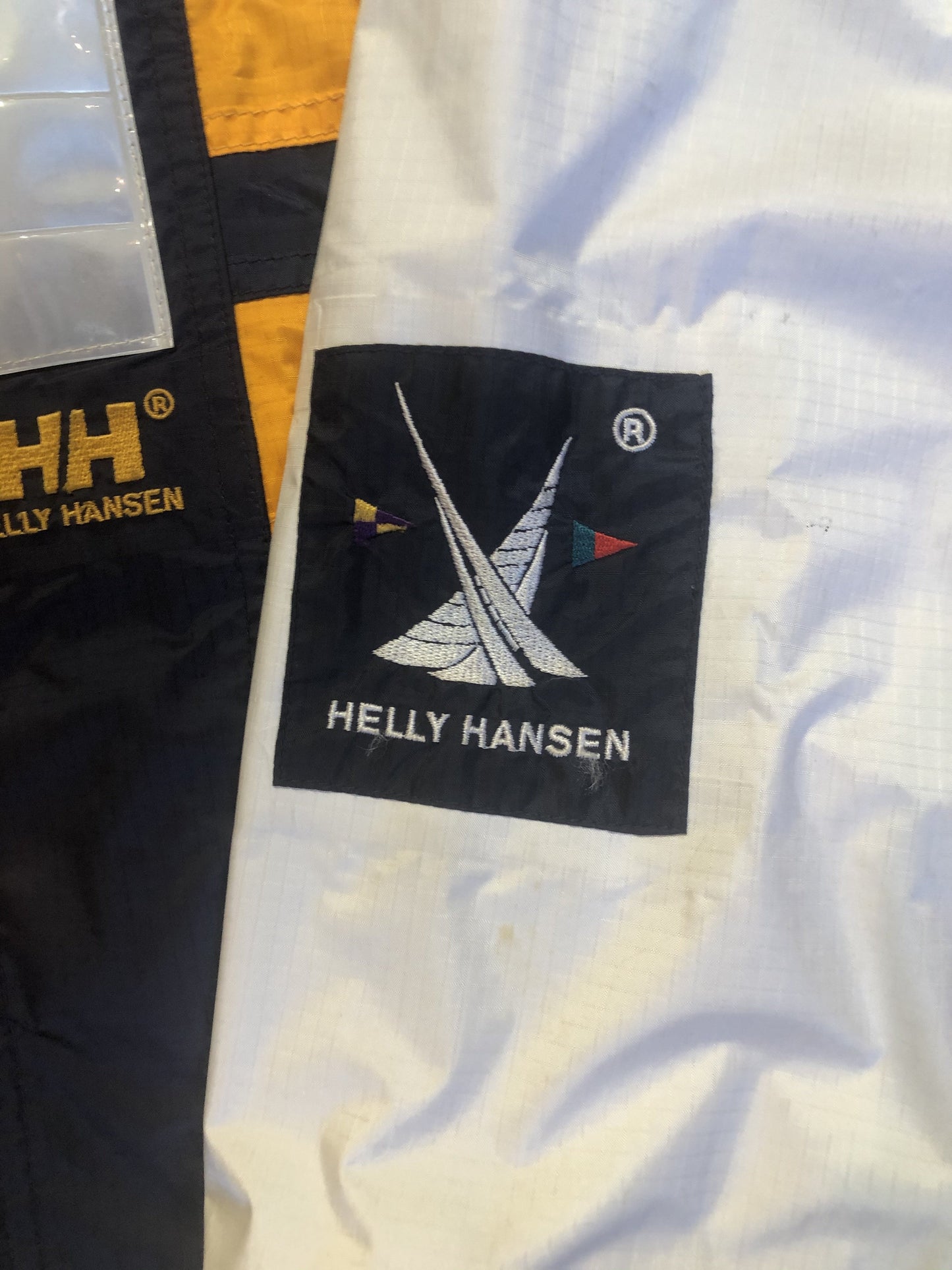 Kingspier Vintage - Heely Hansen ”Extreme” white,yellow and navy windbreaker with funnel neck and roll up hood, zipper and Velcro closures, reflective square on front and Helly Hansen patch on arm. Size XL.
