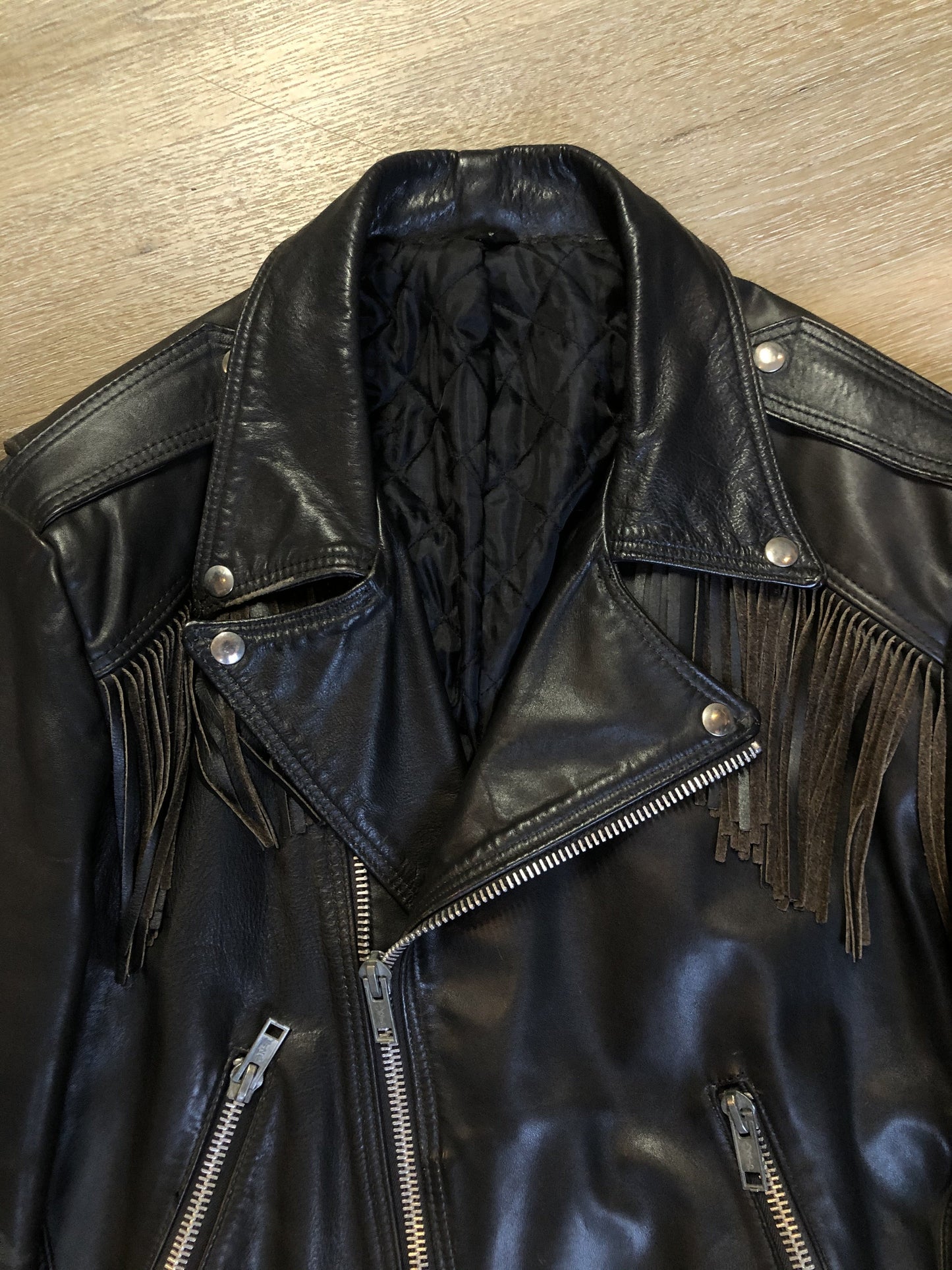 Kingspier Vintage - Action black leather motorcycle jacket with fringe detail and belt at waist. Zipper closure and zip slash pockets, quilted lining with inside pocket. Made in Canada. Size 40.