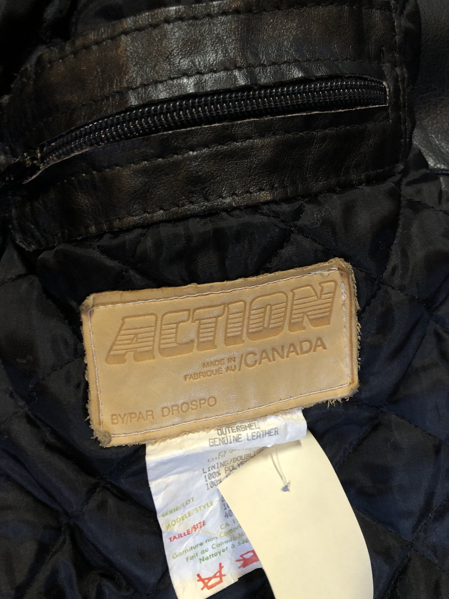Kingspier Vintage - Action black leather motorcycle jacket with fringe detail and belt at waist. Zipper closure and zip slash pockets, quilted lining with inside pocket. Made in Canada. Size 40.