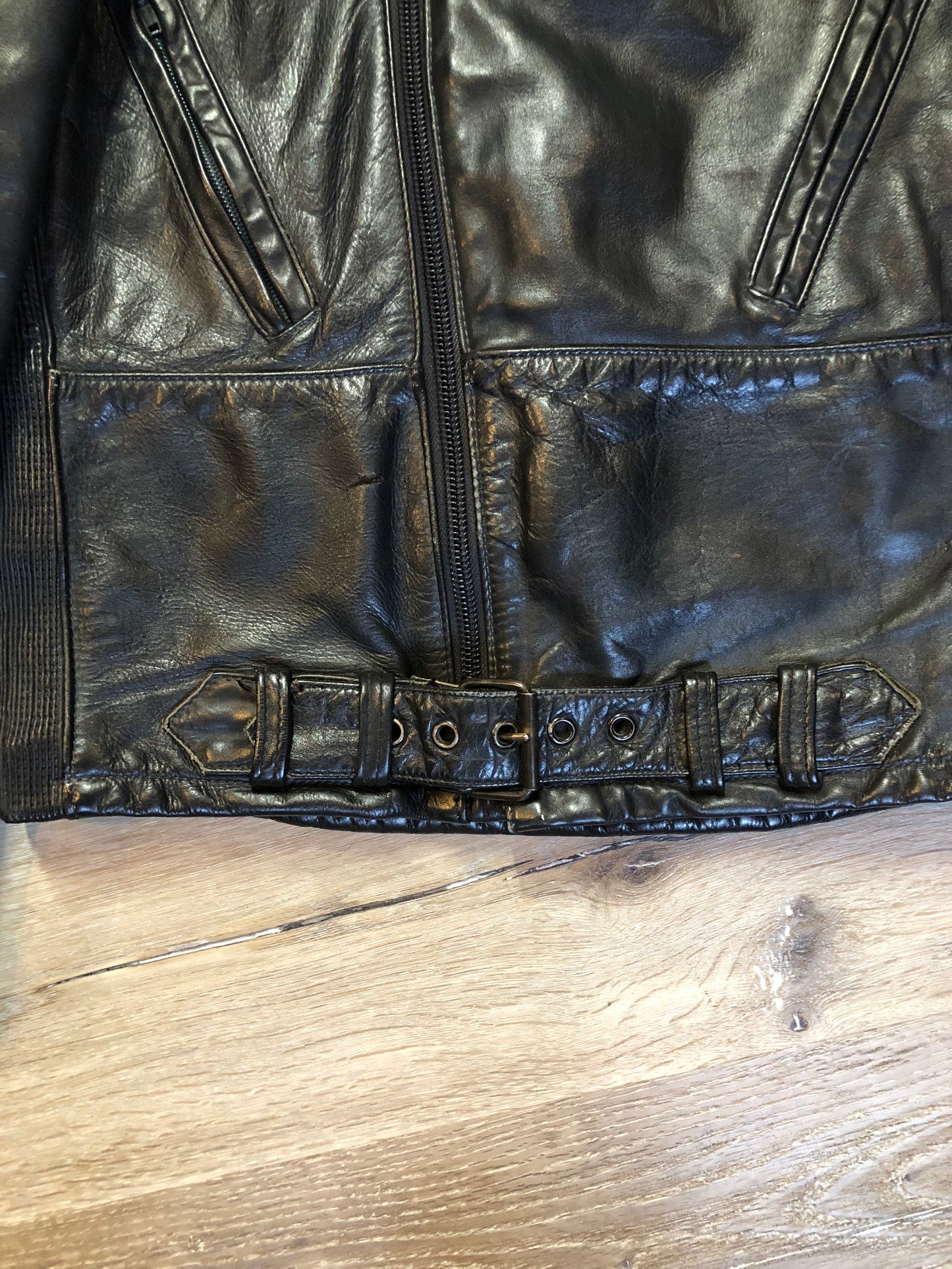 Kingspier Vintage - Taurus by Drospo black leather moto jacket with stretch detailing on the sides and a belt at the waist, zipper down the front, standing collar with Velcro strap, slash pockets and a quilted lining with inside pocket. Size 38. Made in Canada.