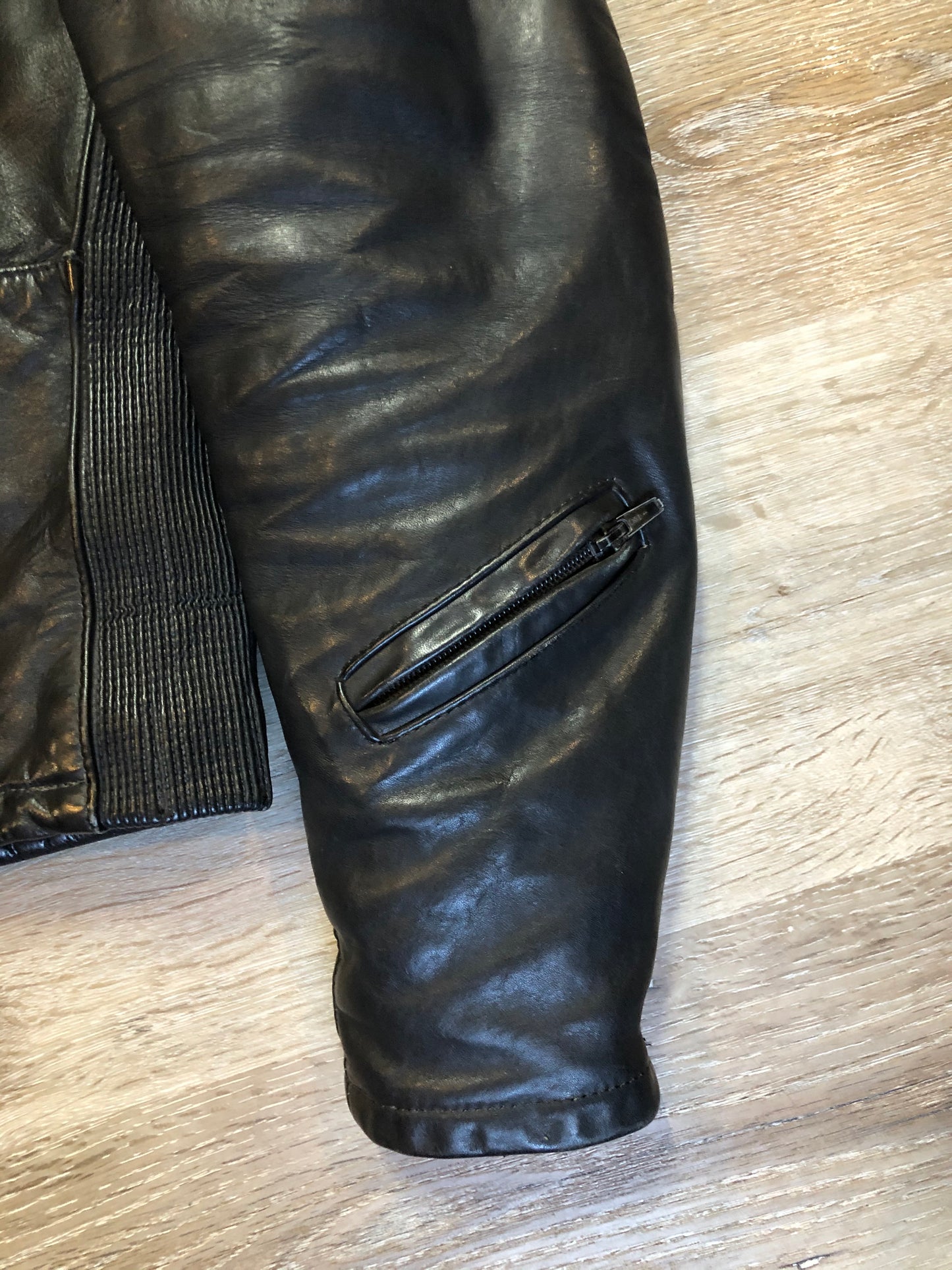 Kingspier Vintage - Taurus by Drospo black leather moto jacket with stretch detailing on the sides and a belt at the waist, zipper down the front, standing collar with Velcro strap, slash pockets and a quilted lining with inside pocket. Size 38. Made in Canada.