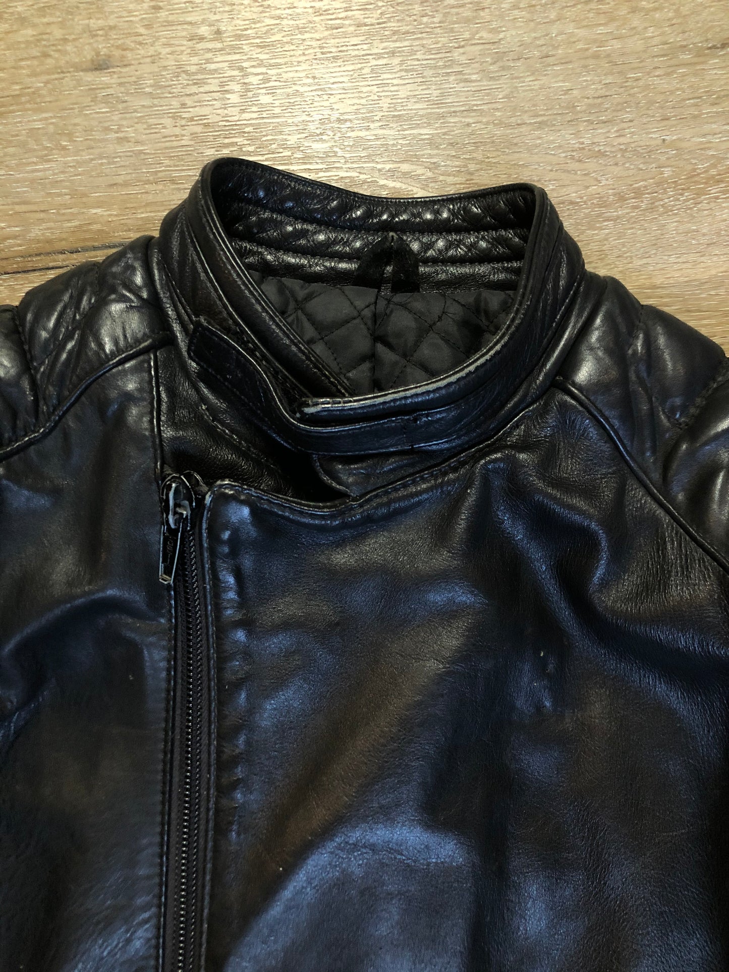 Kingspier Vintage - Taurus by Drospo black leather moto jacket with stretch detailing on the sides and a belt at the waist, zipper down the front, standing collar with Velcro strap, slash pockets and a quilted lining with inside pocket. Size 38. Made in Canada.