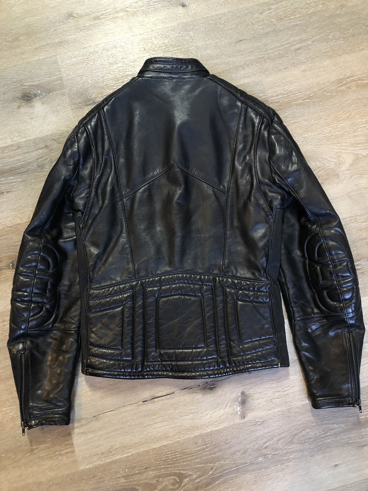 Kingspier Vintage - Taurus by Drospo black leather moto jacket with stretch detailing on the sides and a belt at the waist, zipper down the front, standing collar with Velcro strap, slash pockets and a quilted lining with inside pocket. Size 38. Made in Canada.