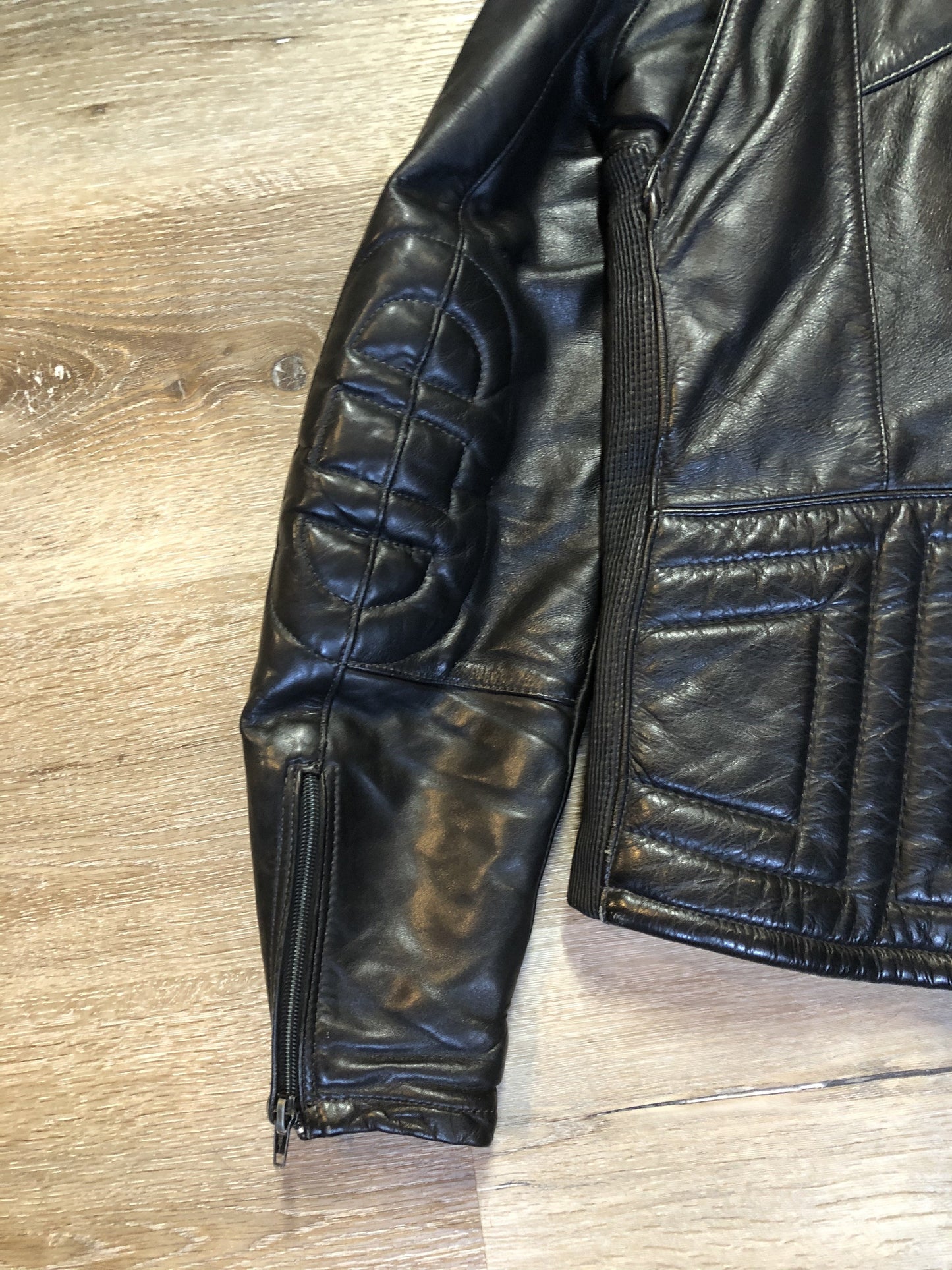 Kingspier Vintage - Taurus by Drospo black leather moto jacket with stretch detailing on the sides and a belt at the waist, zipper down the front, standing collar with Velcro strap, slash pockets and a quilted lining with inside pocket. Size 38. Made in Canada.
