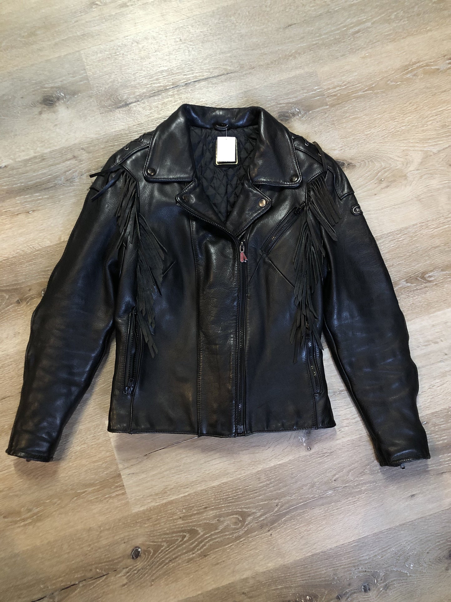 Kingspier Vintage - Hein Gericks black leather motorcycle jacket with fringe detail, zipper, vertical zip pockets lace-up shoulder detail, a quilted lining with inside pocket. Fits Small.