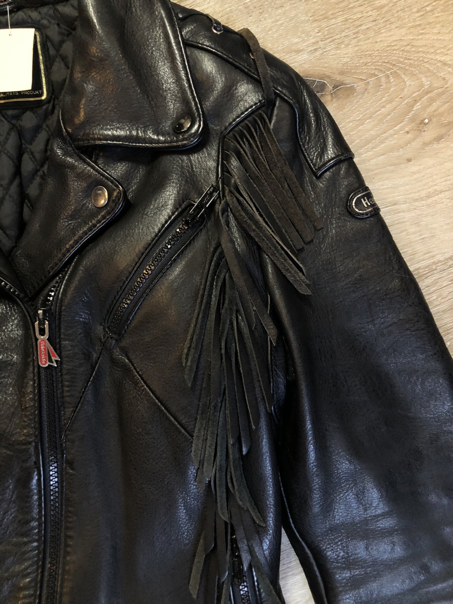 Kingspier Vintage - Hein Gericks black leather motorcycle jacket with fringe detail, zipper, vertical zip pockets lace-up shoulder detail, a quilted lining with inside pocket. Fits Small.