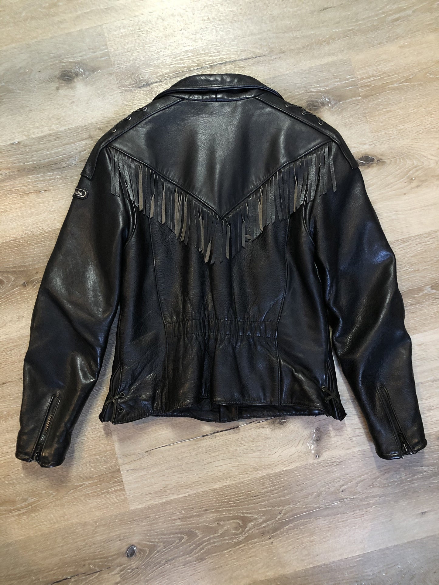 Kingspier Vintage - Hein Gericks black leather motorcycle jacket with fringe detail, zipper, vertical zip pockets lace-up shoulder detail, a quilted lining with inside pocket. Fits Small.