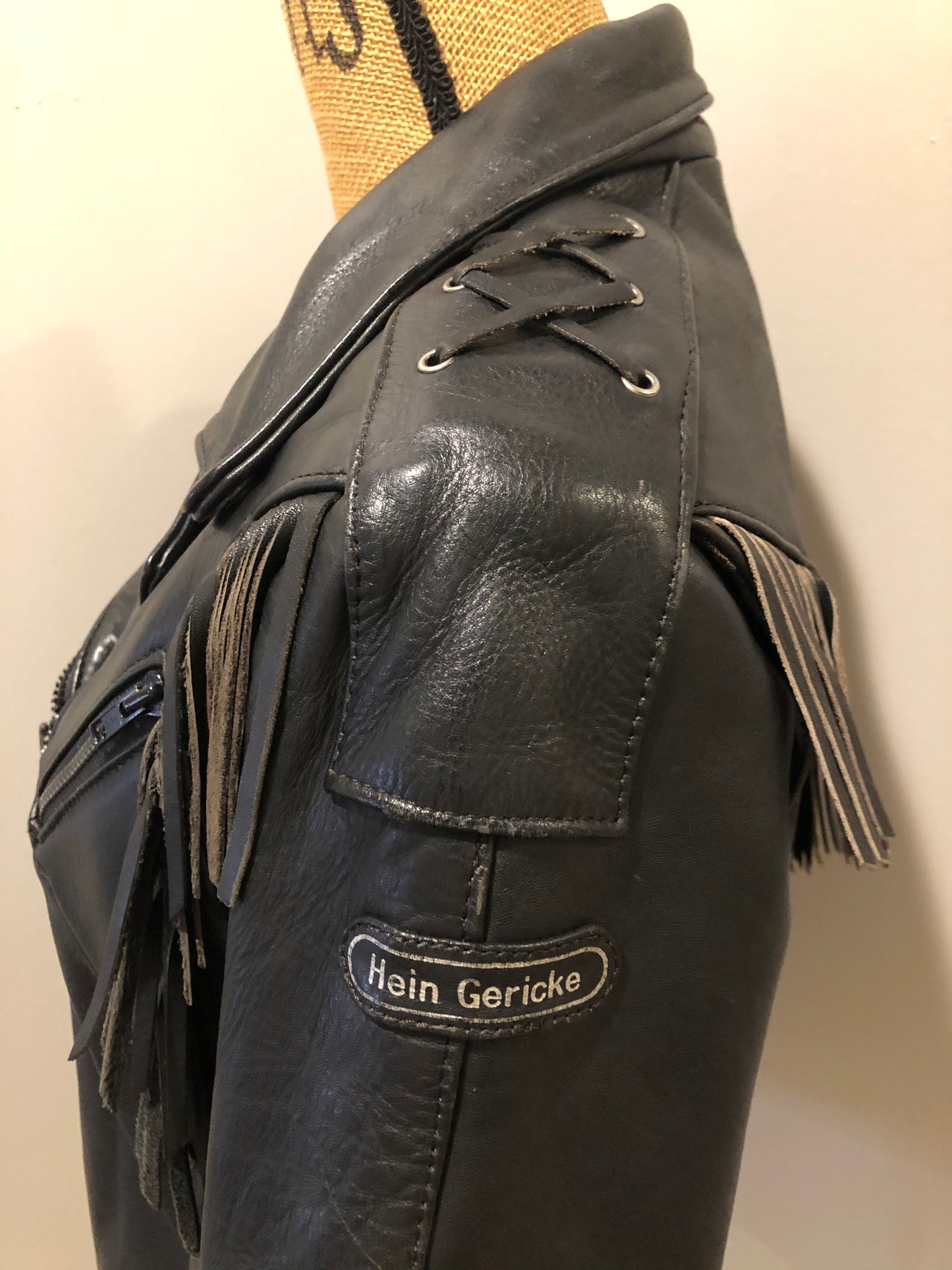 Kingspier Vintage - Hein Gericks black leather motorcycle jacket with fringe detail, zipper, vertical zip pockets lace-up shoulder detail, a quilted lining with inside pocket. Fits Small.