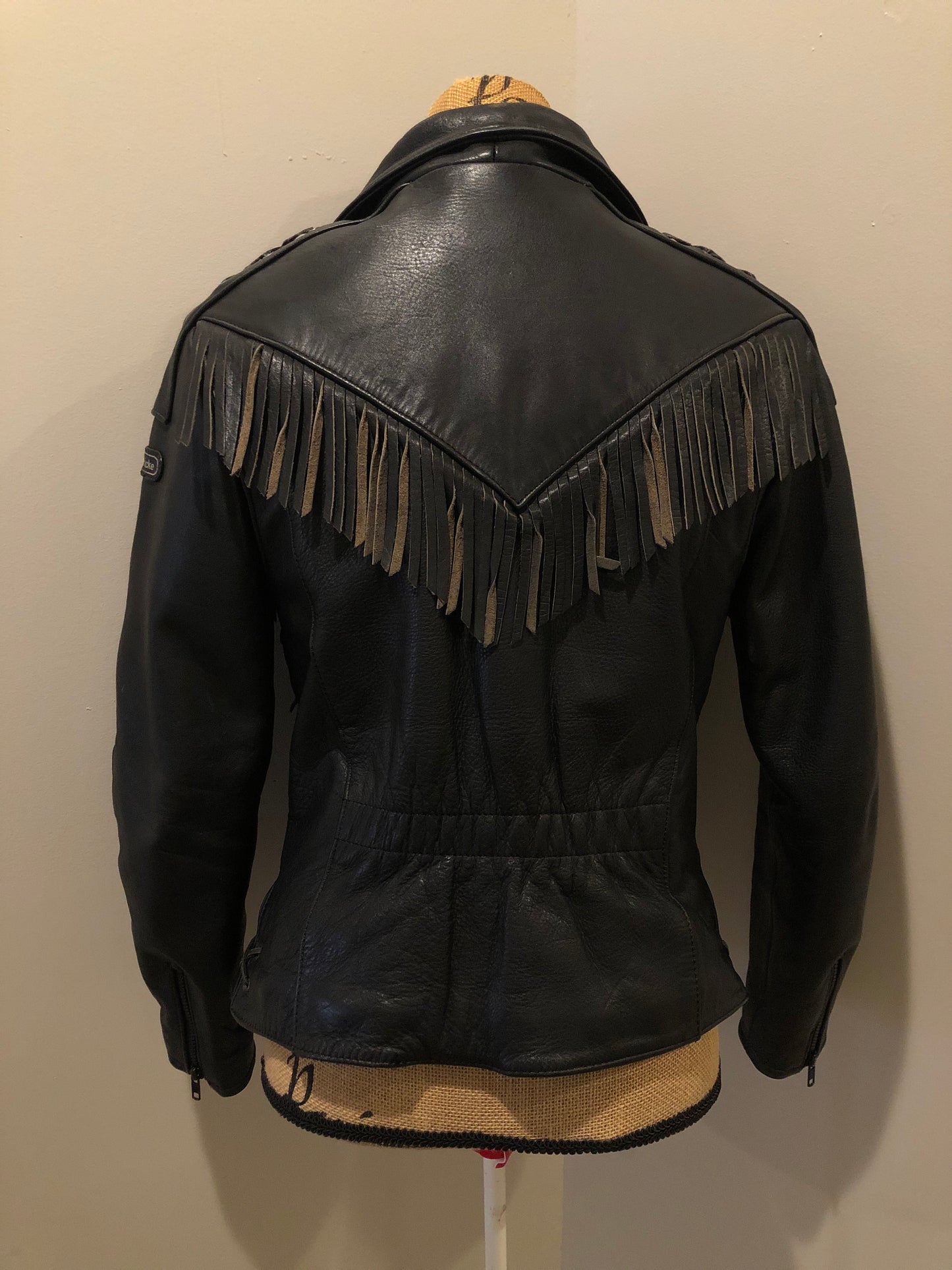 Kingspier Vintage - Hein Gericks black leather motorcycle jacket with fringe detail, zipper, vertical zip pockets lace-up shoulder detail, a quilted lining with inside pocket. Fits Small.