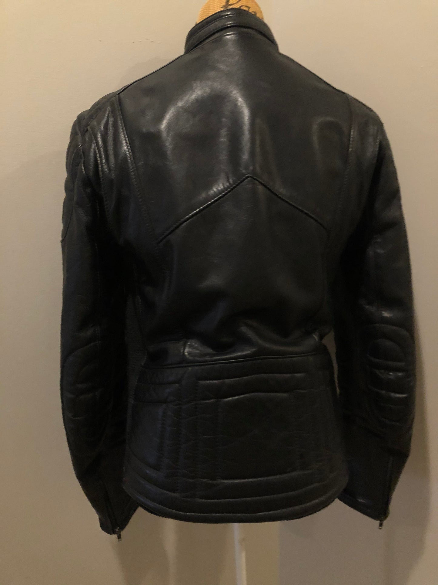 Kingspier Vintage - Taurus by Drospo black leather moto jacket with stretch detailing on the sides and a belt at the waist, zipper down the front, standing collar with Velcro strap, slash pockets and a quilted lining with inside pocket. Size 38. Made in Canada.