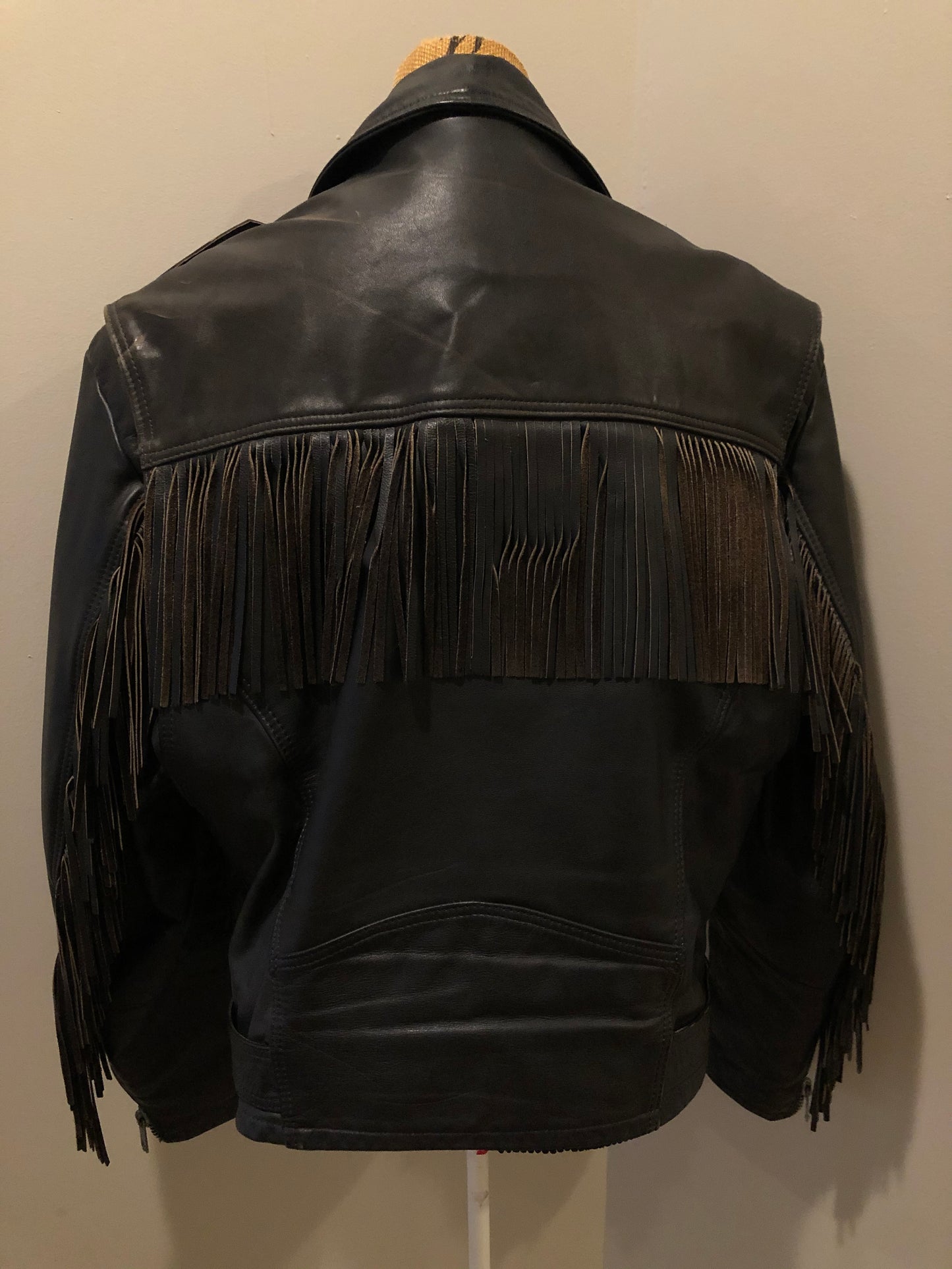 Kingspier Vintage - Action black leather motorcycle jacket with fringe detail and belt at waist. Zipper closure and zip slash pockets, quilted lining with inside pocket. Made in Canada. Size 40.