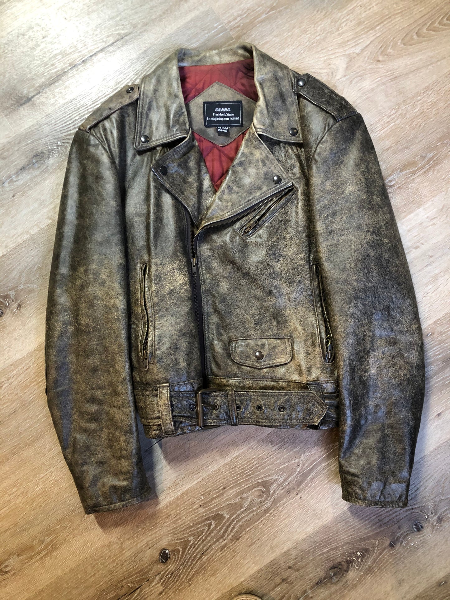 Kingspier Vintage - Sears distressed brown leather motorcycle jacket with zipper, two vertical zip pockets, one flap pocket and a slash pocket on the chest, a belt at the waist and red quilted lining. Size medium.