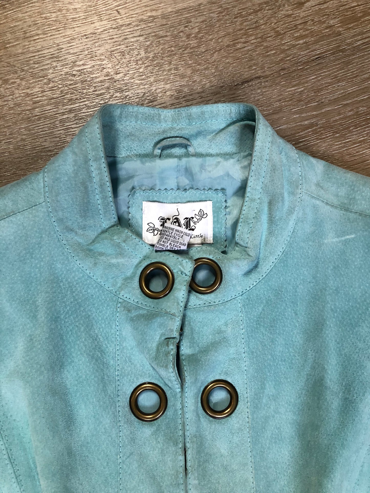 Kingspier Vintage - LAL “Live A LIttle” light teal suede jacket with hidden hook closures, brass grommets running down the front, two zip slash pockets and a small belt at the back. Size large.