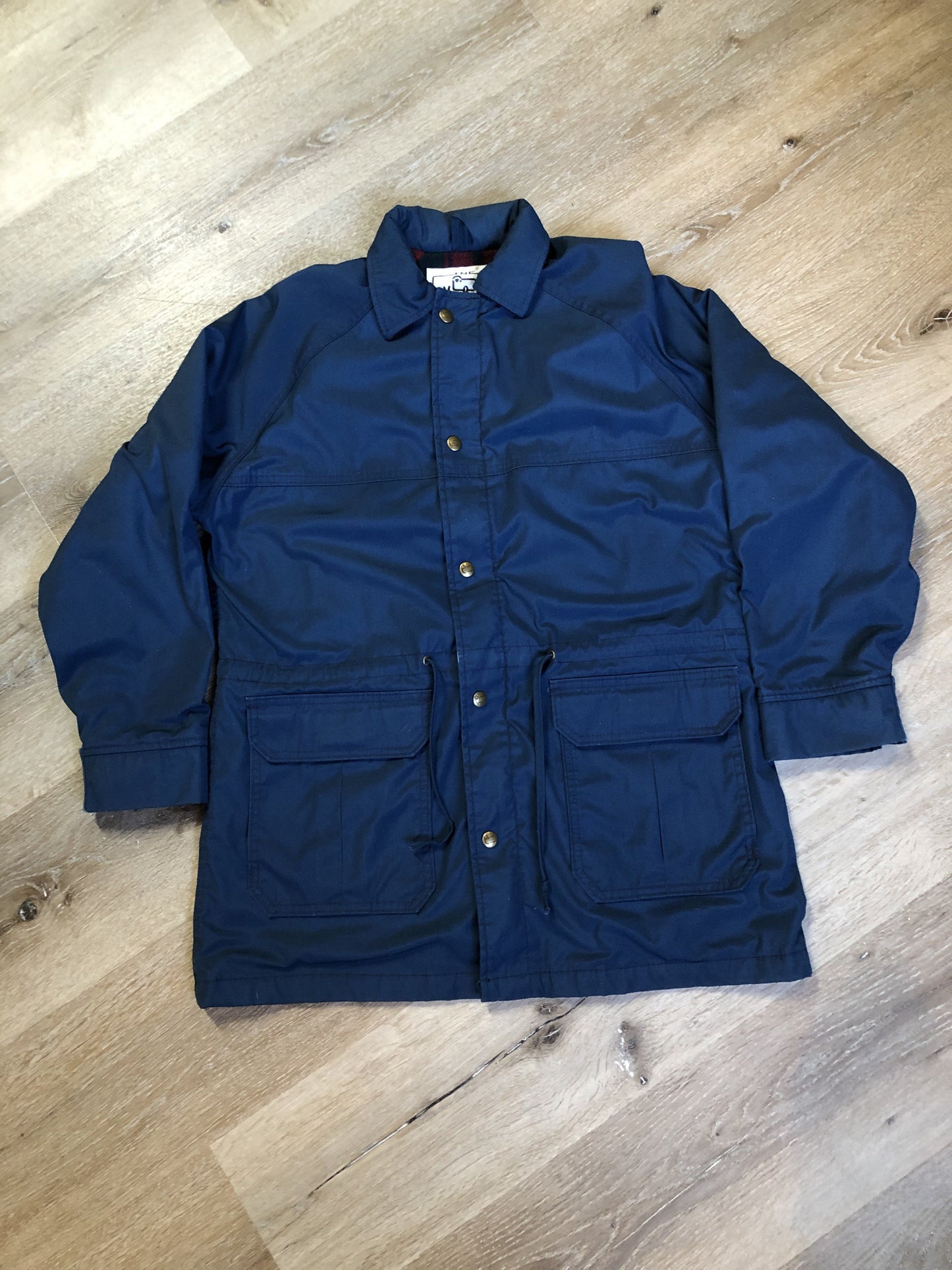 Kingspier Vintage - Woolrich Woman navy jacket with raglan sleeves, hood, zipper, snap closures with sheep logo, two flap pockets, drawstring at waist and red plaid wool lining. Made in the USA. Size medium.
