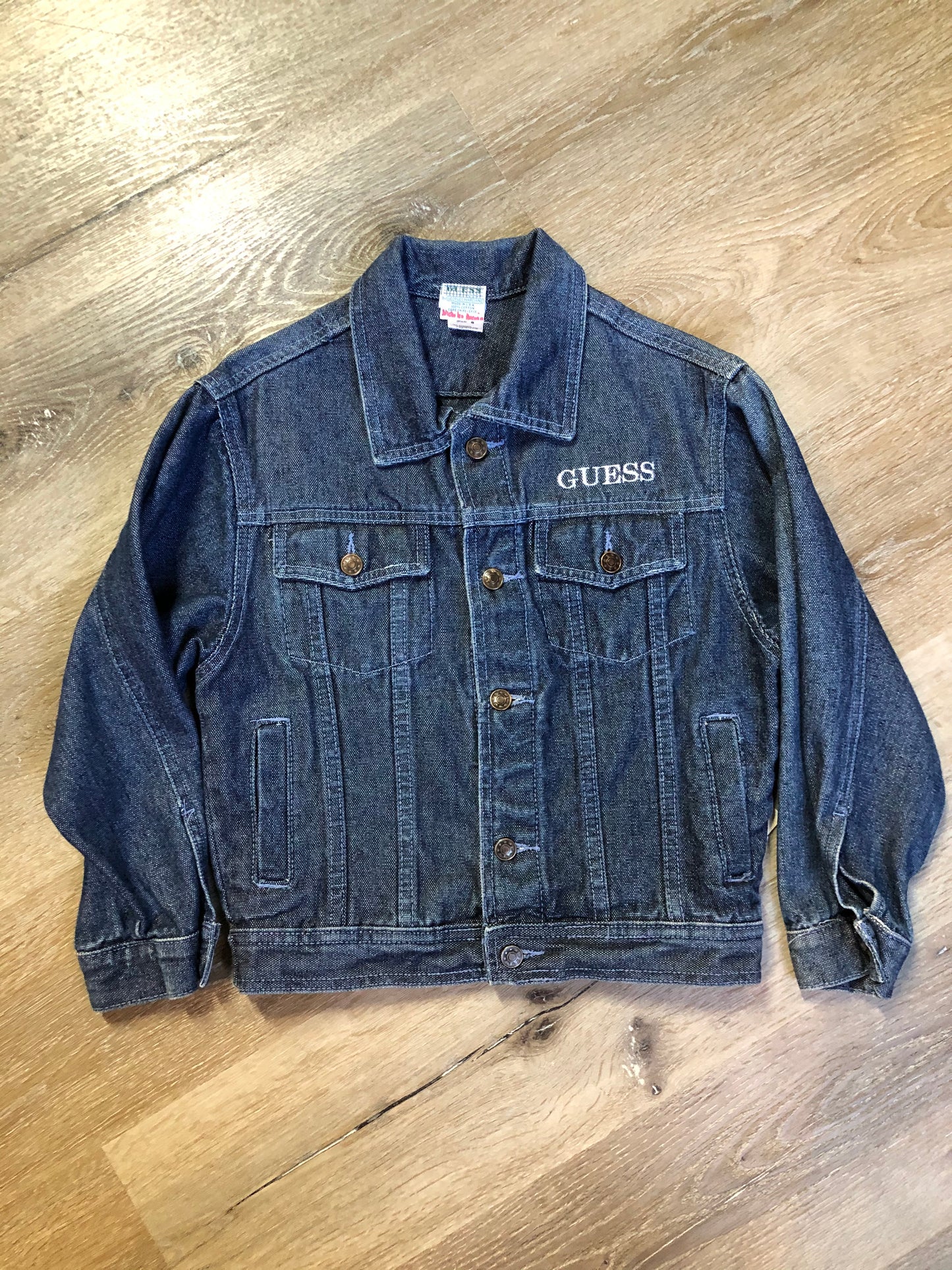 Kingspier Vintage - Guess ‘Georges Marciano’ denim jacket in a medium wash. This jacket features lavender stitching, button closures, two vertical pockets, two flap pockets on the chest and inside pockets. Made in the USA. Size small (fits very small).