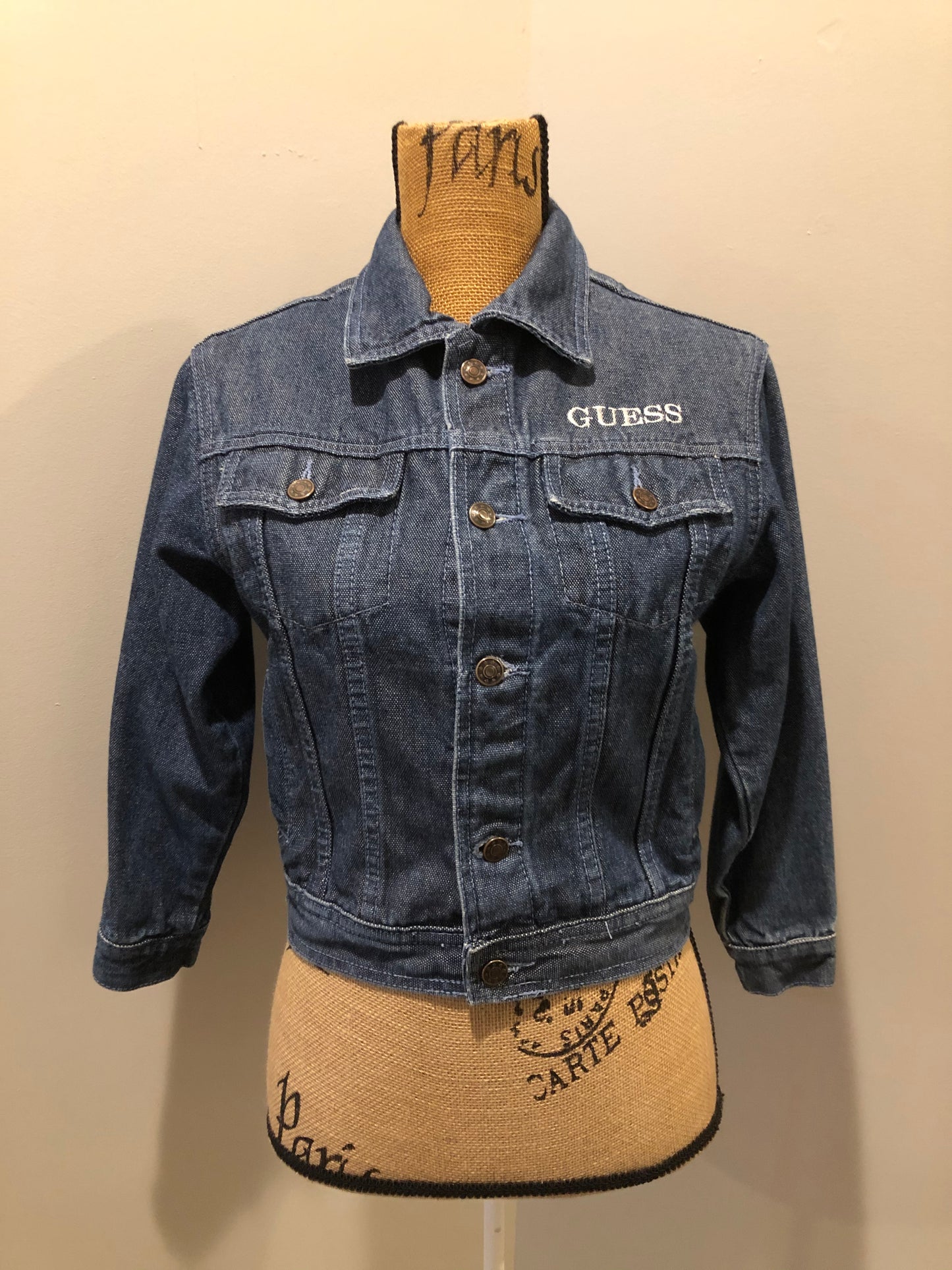 Kingspier Vintage - Guess ‘Georges Marciano’ denim jacket in a medium wash. This jacket features lavender stitching, button closures, two vertical pockets, two flap pockets on the chest and inside pockets. Made in the USA. Size small (fits very small).