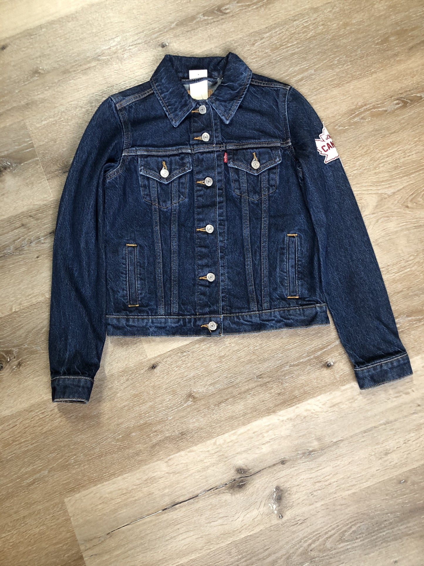 Kingspier Vintage - Levi’s Original Trucker Jacket in a medium wash denim with Canada leaf patch on the left shoulder, button closures, two vertical pockets and two flap pockets on the chest. Size XS.