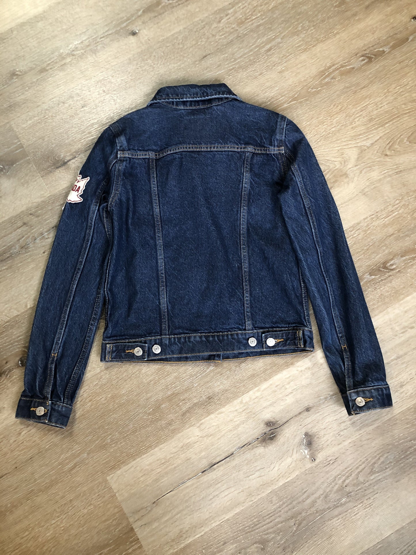 Kingspier Vintage - Levi’s Original Trucker Jacket in a medium wash denim with Canada leaf patch on the left shoulder, button closures, two vertical pockets and two flap pockets on the chest. Size XS.