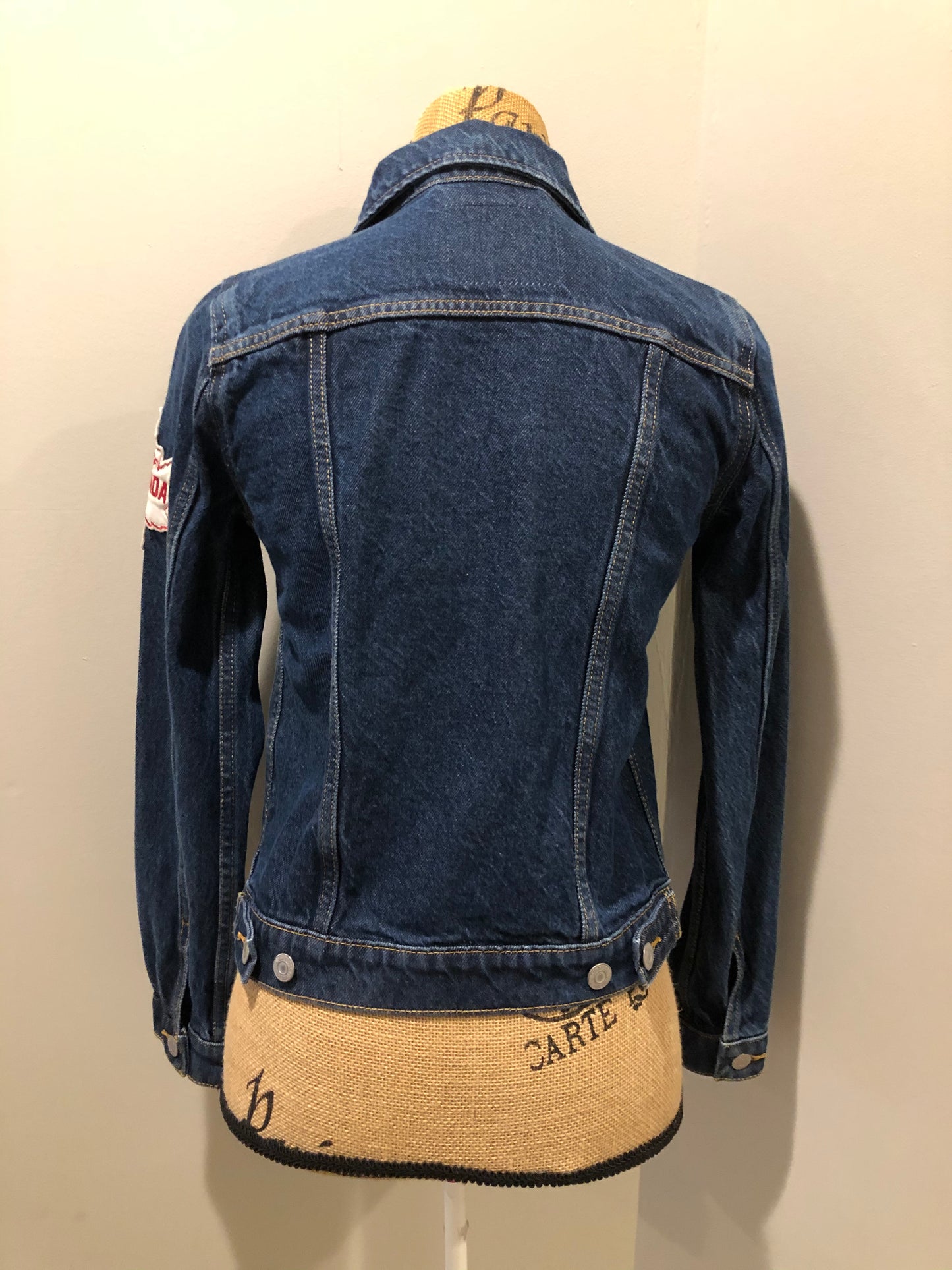 Kingspier Vintage - Levi’s Original Trucker Jacket in a medium wash denim with Canada leaf patch on the left shoulder, button closures, two vertical pockets and two flap pockets on the chest. Size XS.
