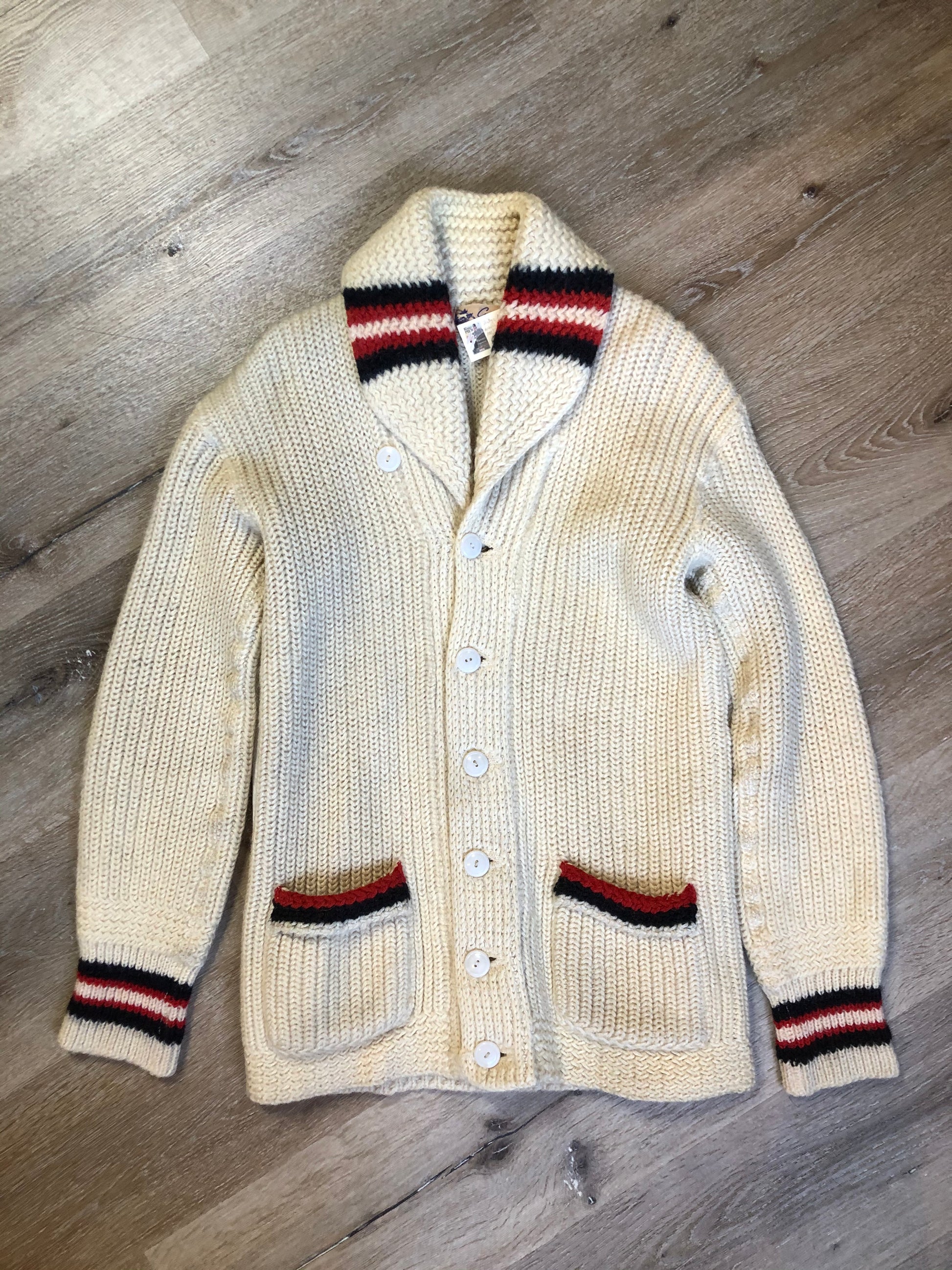 Kingspier Vintage - Curl-Rite by Rice-Knit Sportswear 1950’s curing sweater in cream with red and black strip details, shawl collar, button closures and pockets. 100% wool. Size medium. Made in Nova Scotia.
