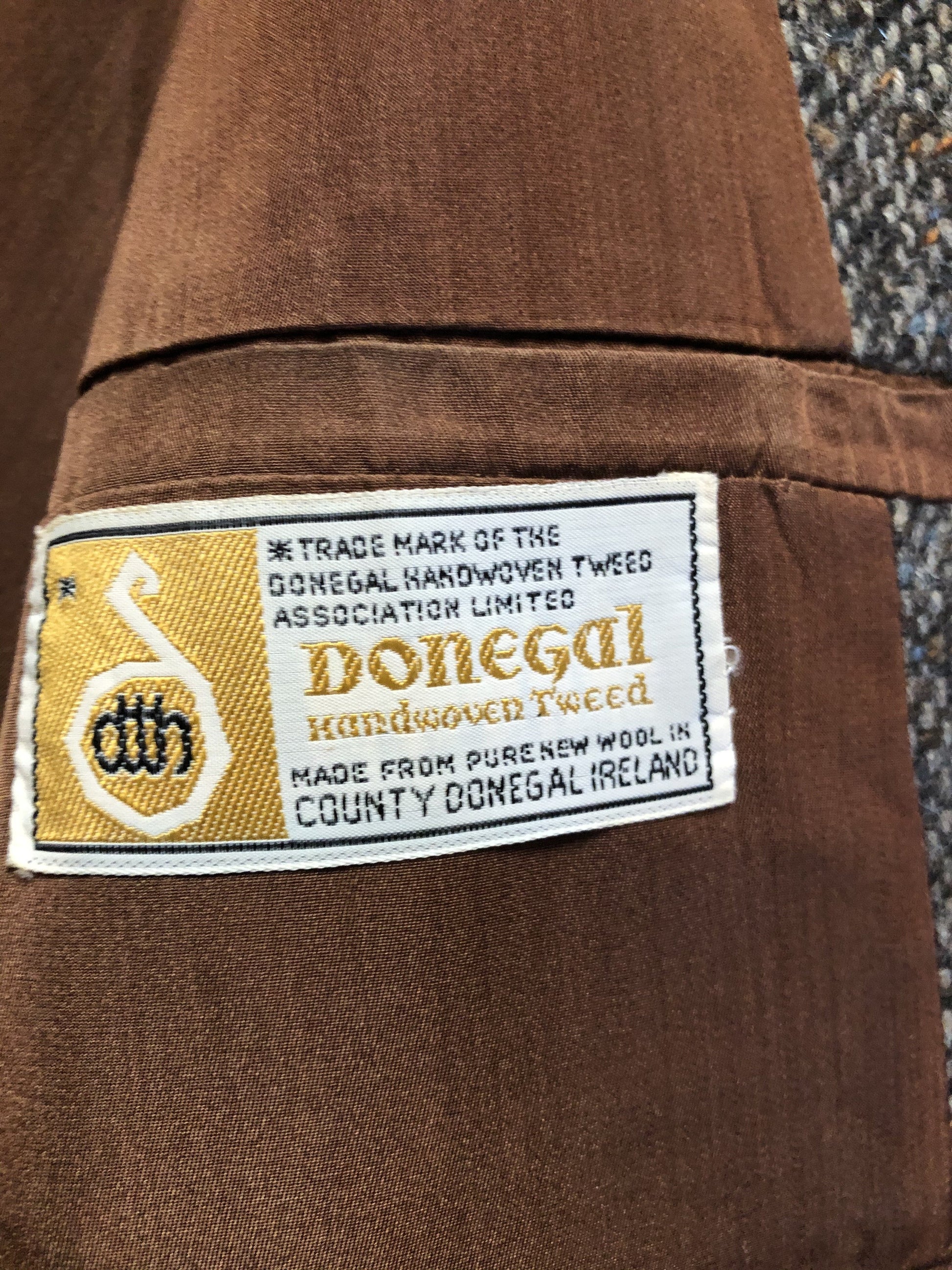 Kingspier Vintage - Donegal handwoven grey with blue and orange flecks 100% wool tweed jacket. This jacket is a two button, notch lapel with two patch pockets, a breast pocket and two inside pockets and a “this I defend” emblem embroidered on the chest. Made in Ireland.