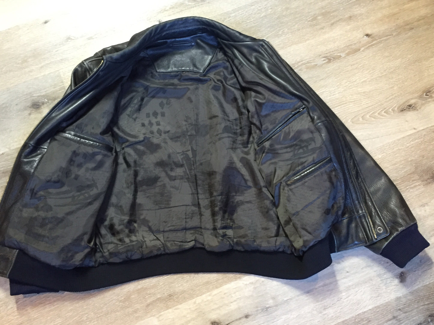 Kingspier Vintage - Black leather pilot jacket with zipper and snap closures, flap pockets, knit trim, inside pocket and plane pattern on inside lining. Size large.