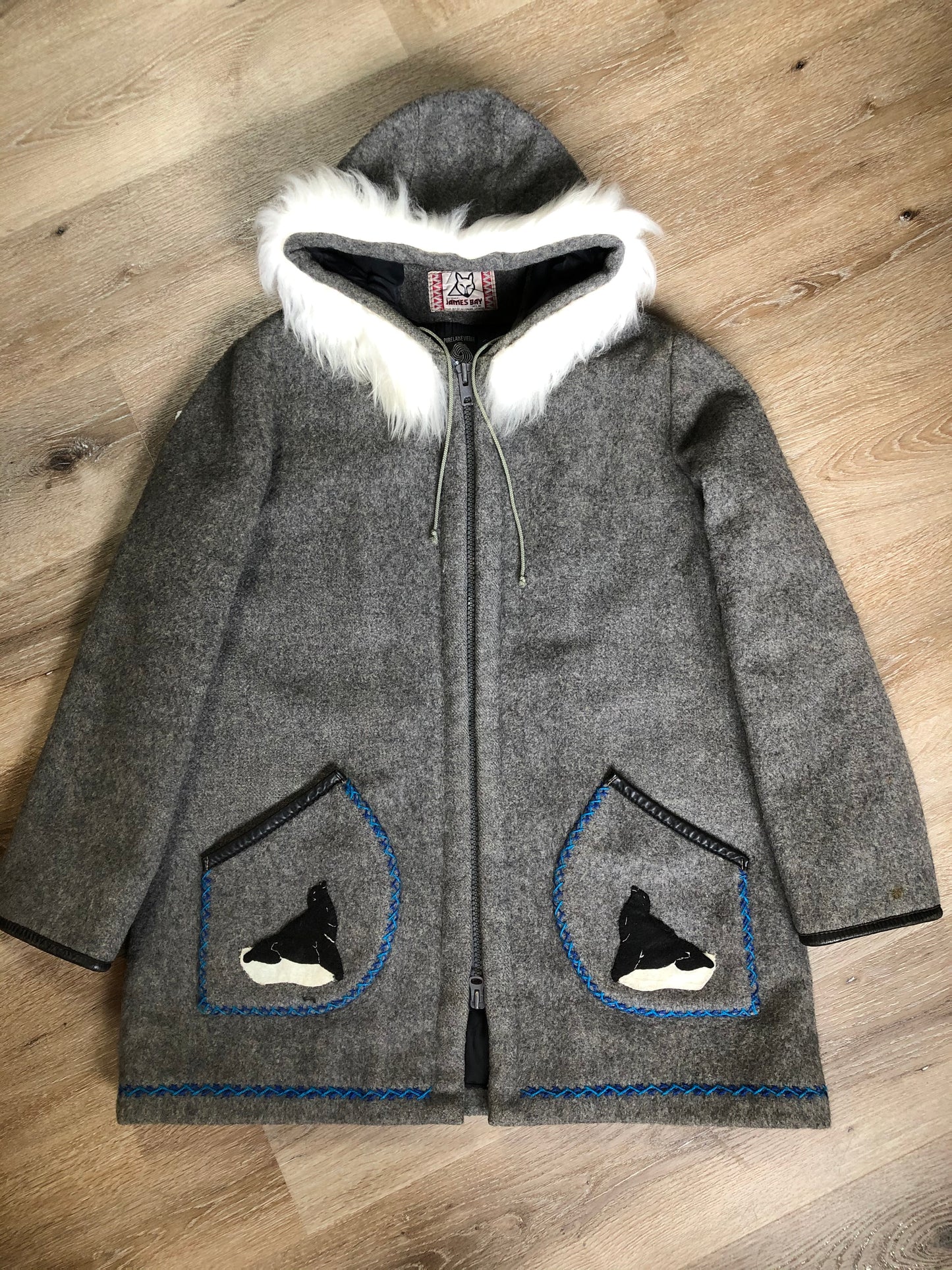 Kingspier Vintage - James Bay pure virgin wool northern parka in grey. This parka features a hood with white faux fur trim, zipper closure, quilted lining, knit inside hidden cuffs, hand stitched detail around the patch pockets and hem, felt seal appliqués in the front and a lovely arctic landscape on the back. Made in Canada.