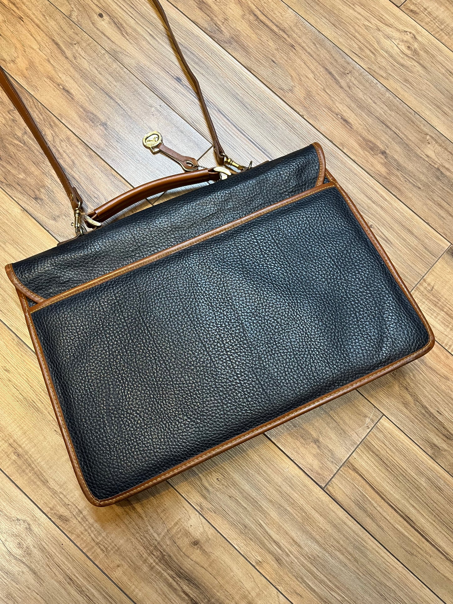 Dooney and Burke all weather leather briefcase in navy with top handle, shoulder strap and brass hardware.
