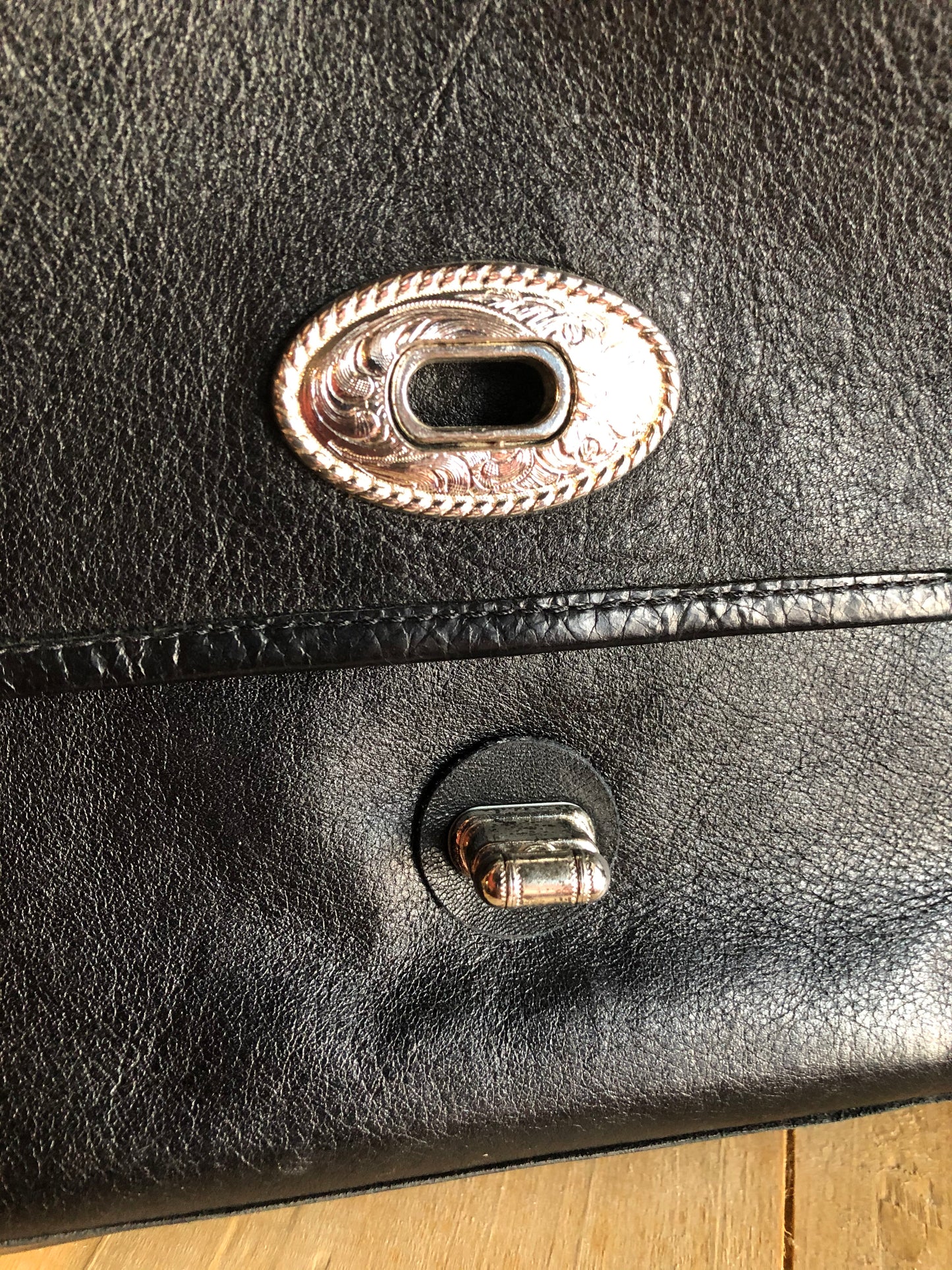 Kingspier Vintage - Black leather satchel with ornate front closure, lined in maroon coloured leather and features many inside pockets.