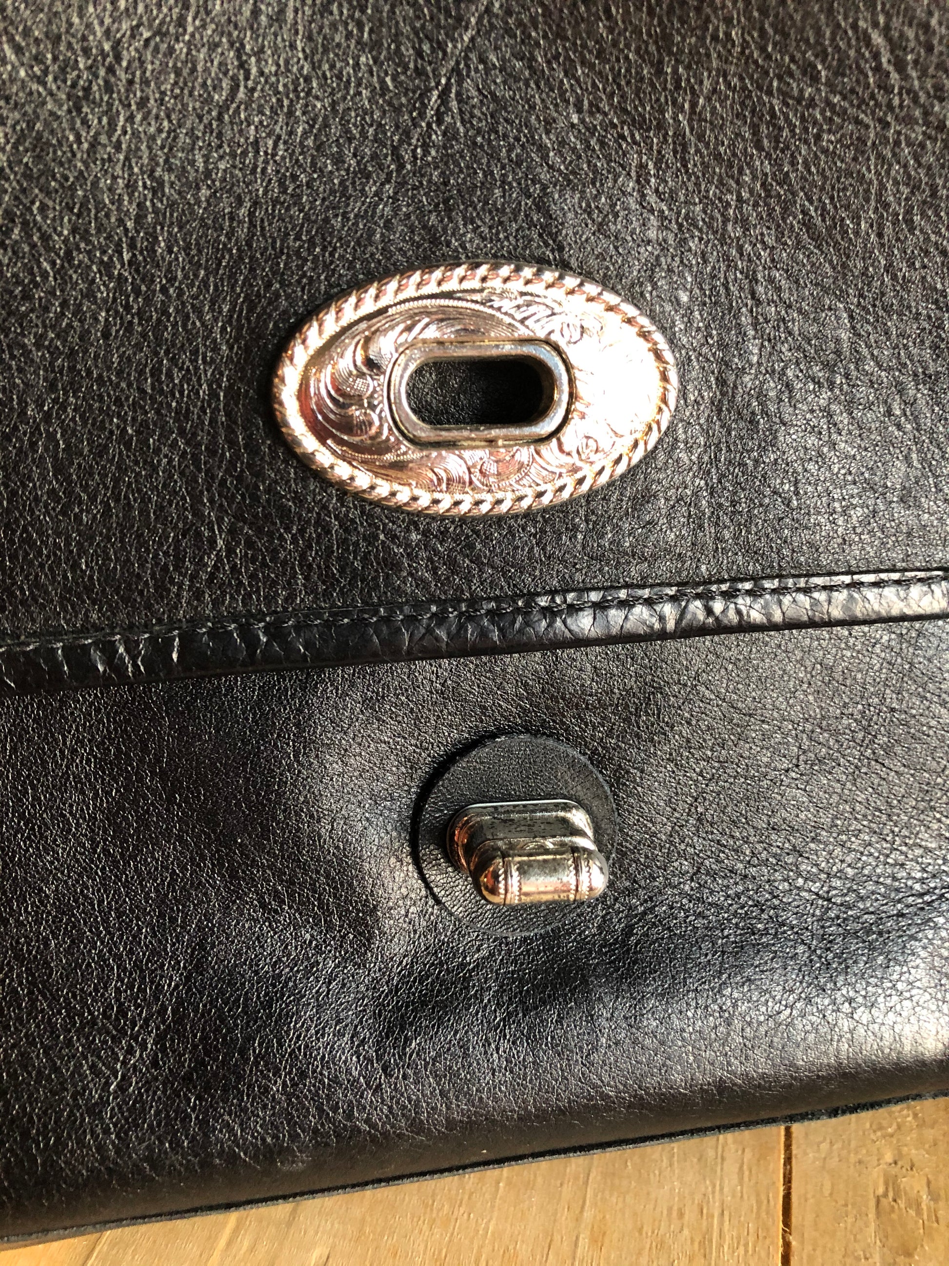 Kingspier Vintage - Black leather satchel with ornate front closure, lined in maroon coloured leather and features many inside pockets.