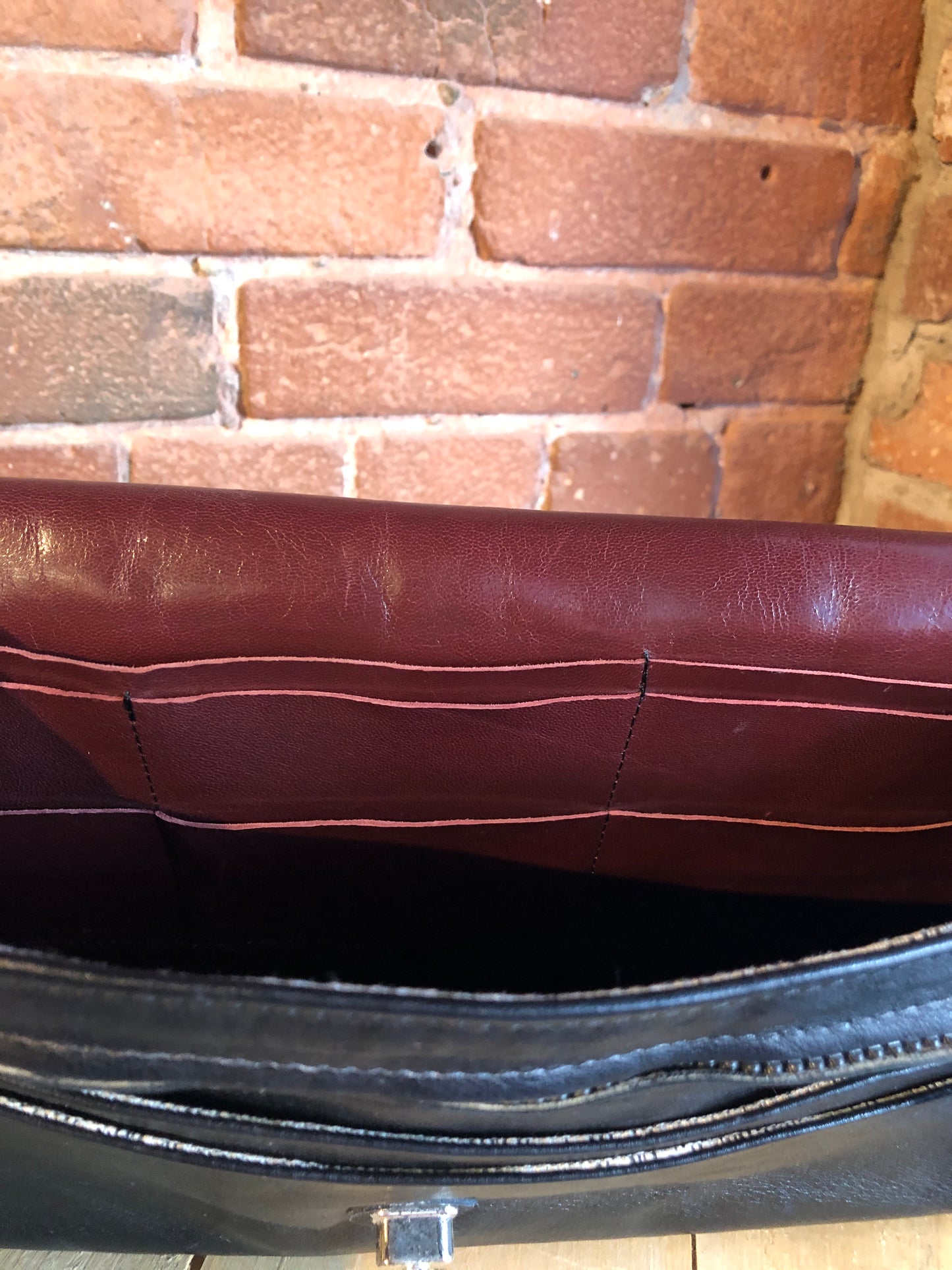 Kingspier Vintage - Black leather satchel with ornate front closure, lined in maroon coloured leather and features many inside pockets.