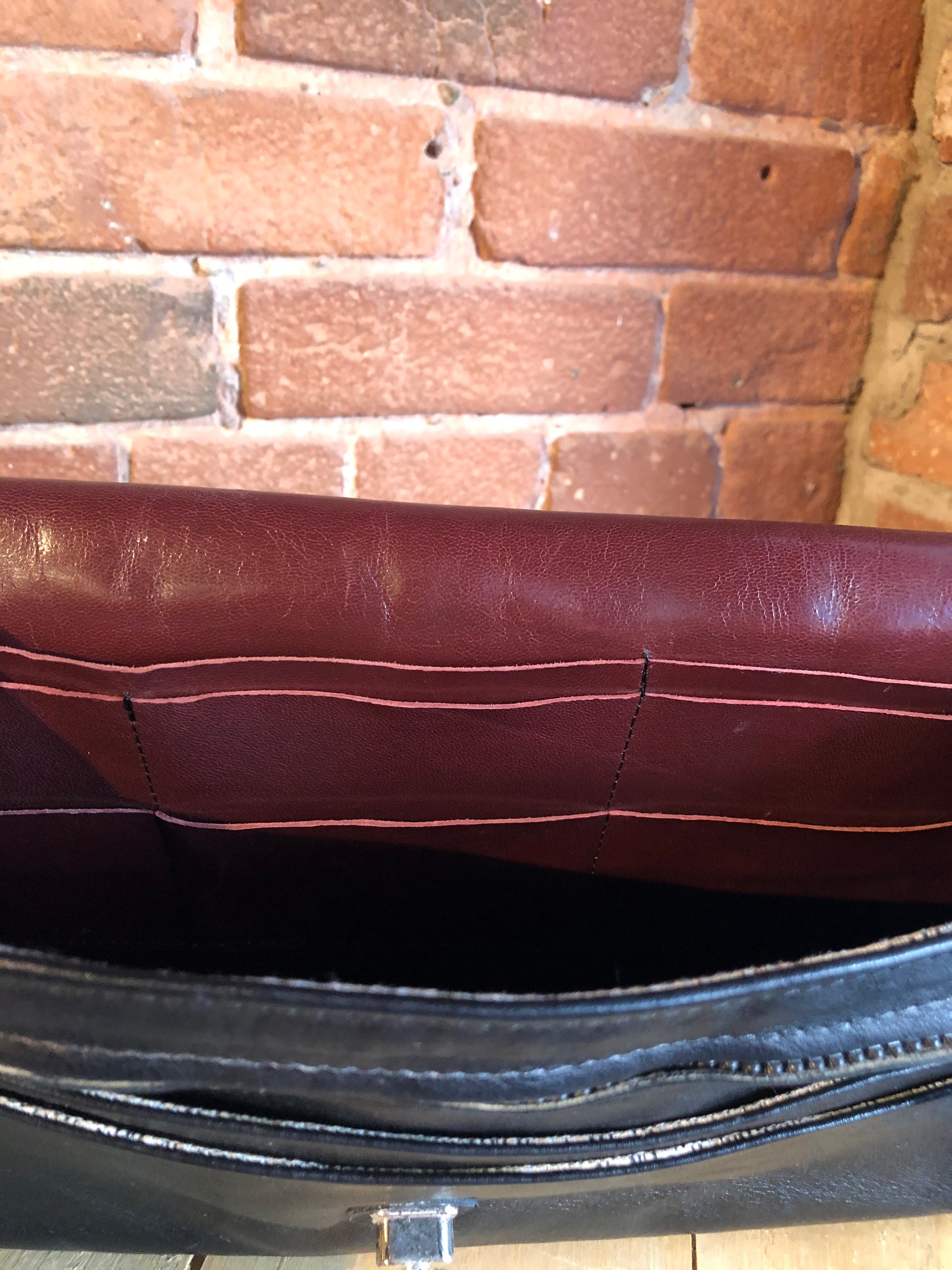 Kingspier Vintage - Black leather satchel with ornate front closure, lined in maroon coloured leather and features many inside pockets.