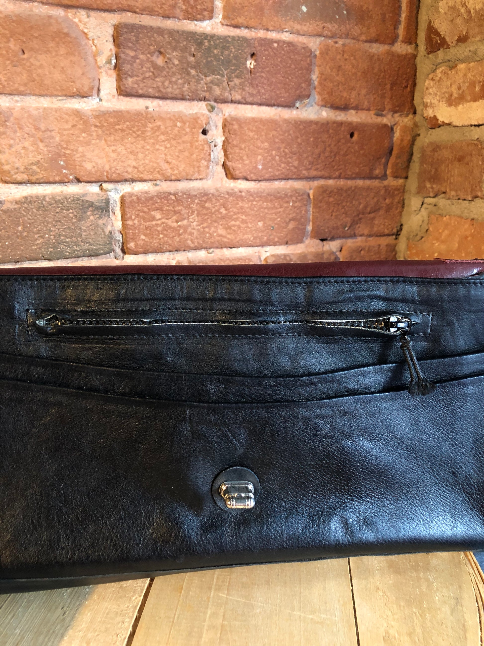 Kingspier Vintage - Black leather satchel with ornate front closure, lined in maroon coloured leather and features many inside pockets.