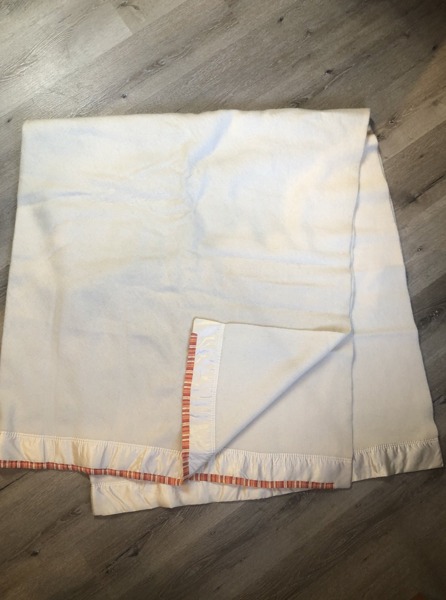 Kingspier Vintage - White 100% wool blanket with white ribbon trim on one end and a red, yellow and orange striped ribbon on the other end.
Fits a double bed.