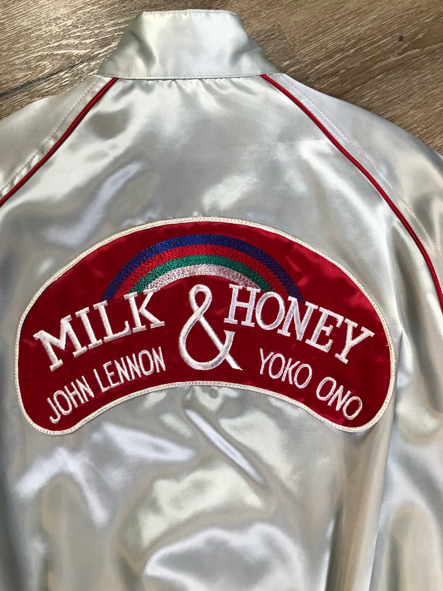Kingspier Vintage - Milk and Honey - John Lennon and Yoko Ono Roadie Tour Jacket from the mid 1980’s. A very rare collectors piece from John Lennon’s last studio album. Jacket is light grey nylon with satin effect with two slash pockets, elastic waist and cuffs, chunky red zip up front with popper at the collar. The jacket features a star logo on the front and Milk and honey logo on the back with a rainbow. Made in the USA. Size XS.