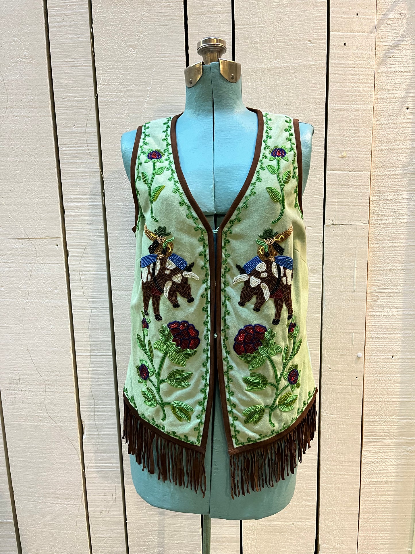 Double D Ranch light green goat suede vest with brown fringe detail, hook and eye closure, cotton/ linen back panel, satin lining and a western cowboy and desert rose design that is hand beaded.
Made in India
Size Medium