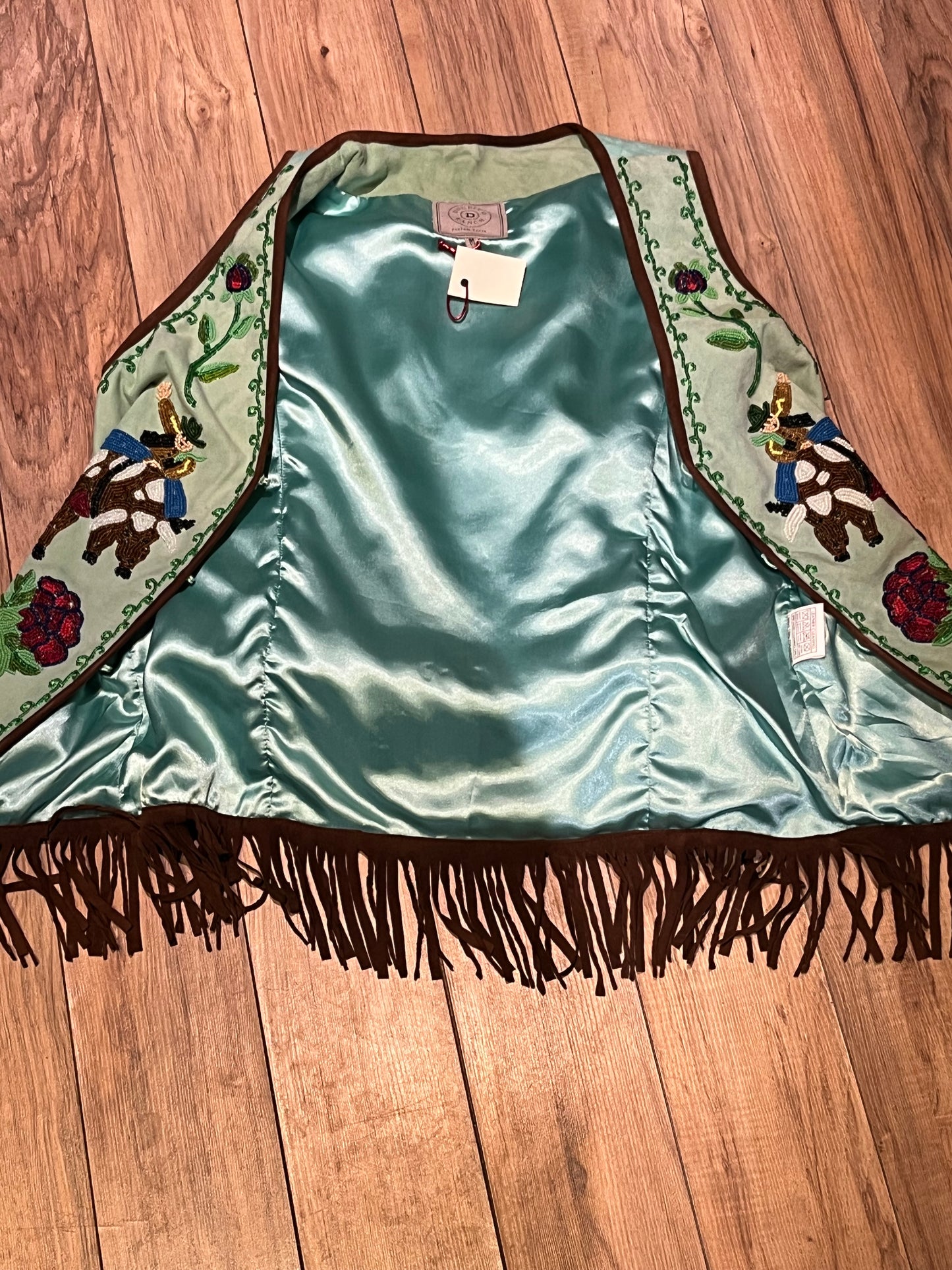 Double D Ranch light green goat suede vest with brown fringe detail, hook and eye closure, cotton/ linen back panel, satin lining and a western cowboy and desert rose design that is hand beaded.
Made in India
Size Medium