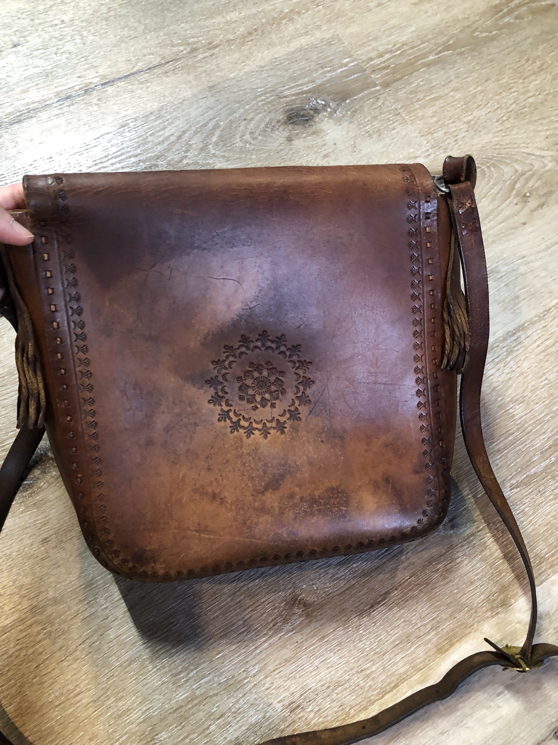 Vintage full grain brown leather crossbody bag with leather fringe, hand tooled designs, brass hardware, flap closure, two interior compartments and adjustable shoulder strap.  Bag is scented with patchouli - Kingspier Vintage