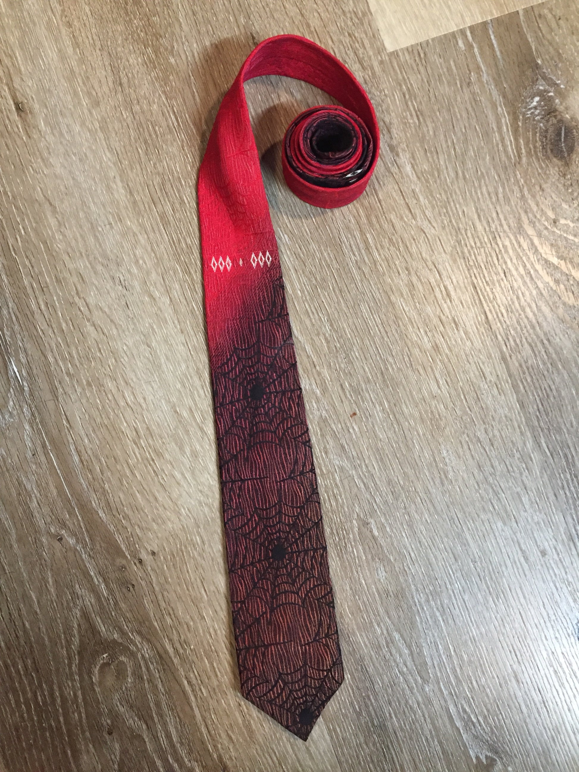 Kingspier Vintage - Abbey red tie with black spider web motif. Fibres unknown.
Length: 55”
Width: 2.5” 
This tie is in excellent condition.