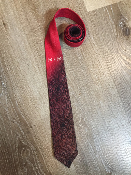 Kingspier Vintage - Abbey red tie with black spider web motif. Fibres unknown.
Length: 55”
Width: 2.5” 
This tie is in excellent condition.