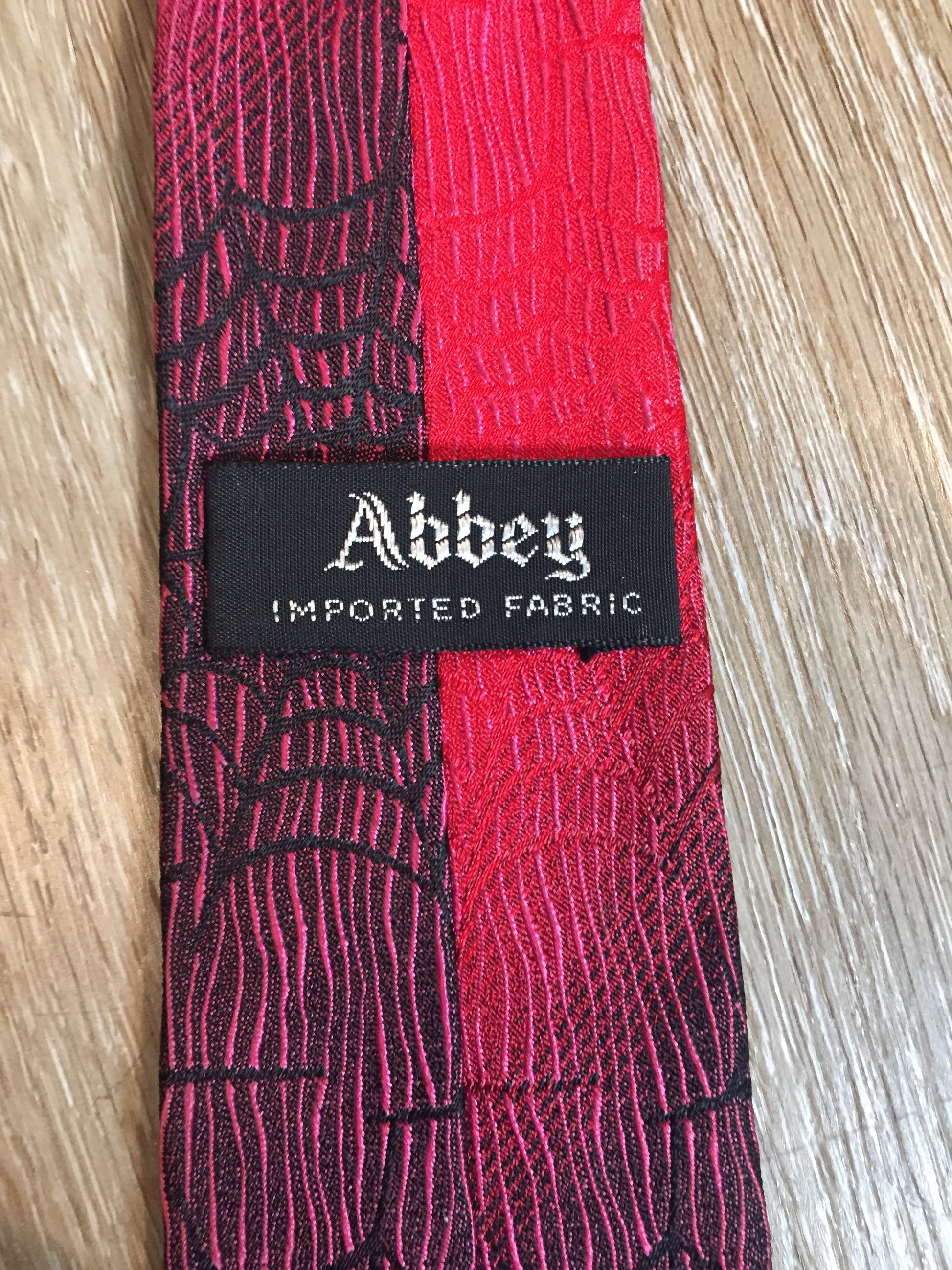 Kingspier Vintage - Abbey red tie with black spider web motif. Fibres unknown.
Length: 55”
Width: 2.5” 
This tie is in excellent condition.