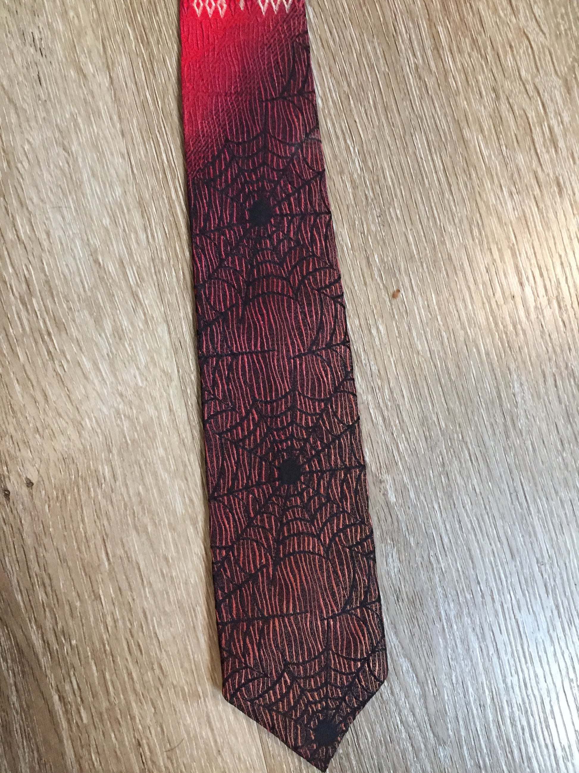Kingspier Vintage - Abbey red tie with black spider web motif. Fibres unknown.
Length: 55”
Width: 2.5” 
This tie is in excellent condition.